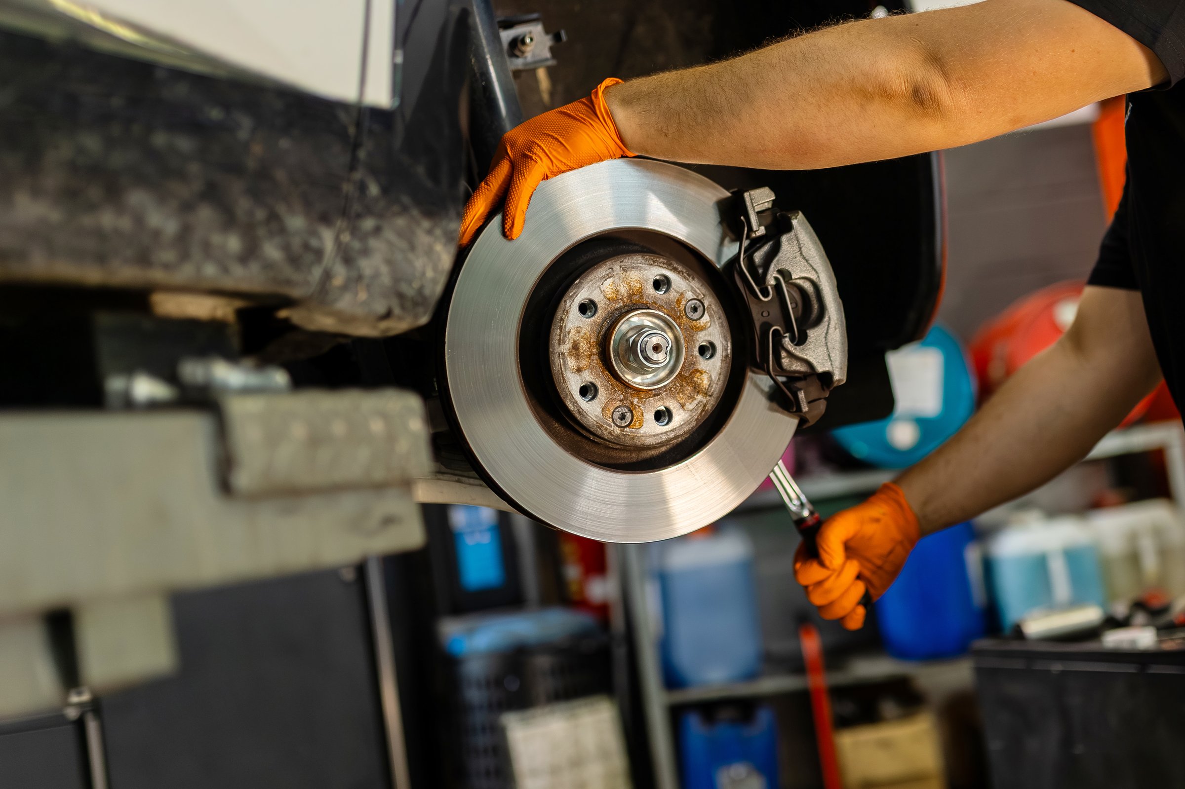 Mechanic hands with orange gloves installing or repairing a car brake disc. Maintenance of the braking system for vehicle safety in the garage.
