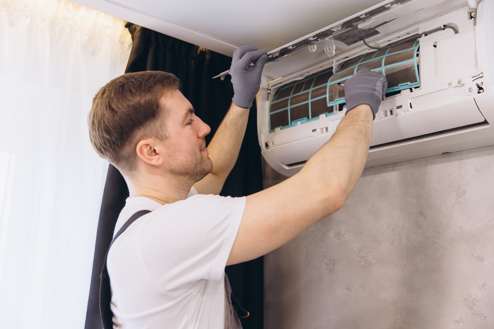 Electrician installing an air conditioner unit on a wall, performing maintenance and cleaning