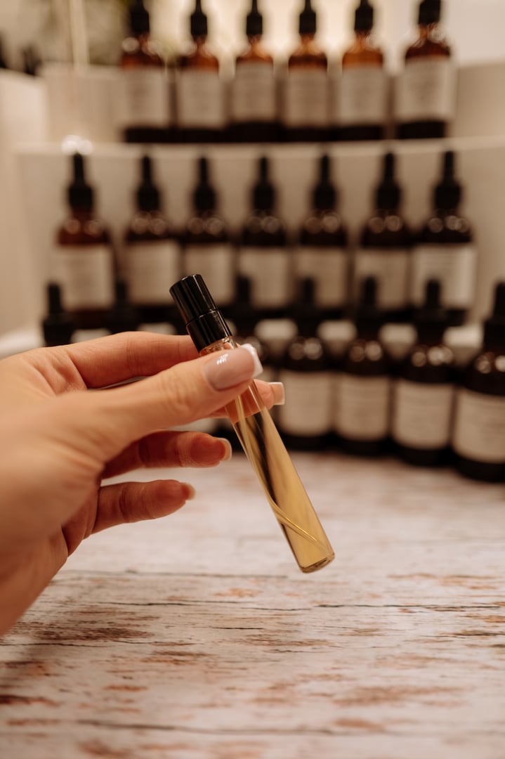 Female hand holding glass perfume tester with gold essential oil, perfumery creation process
