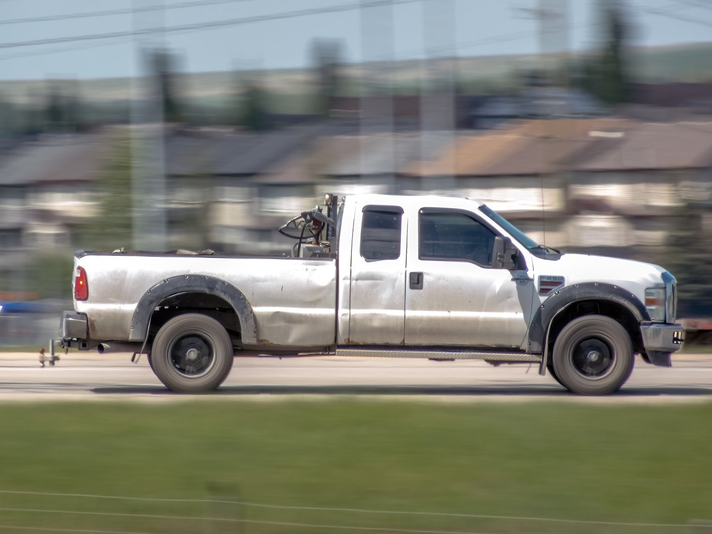 Calgary, Alberta, Canada. Jun 2, 2025. A weathered Ford Super Duty pickup truck, equipped for work, drives with motion blur against a suburban backdrop, symbolizing utilitarian strength.