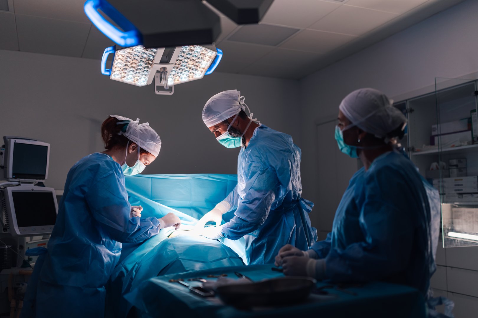 An intricate surgical procedure in progress with healthcare professionals in full surgical gear, under bright operating room lights, emphasizing the modern medical equipment and organization.