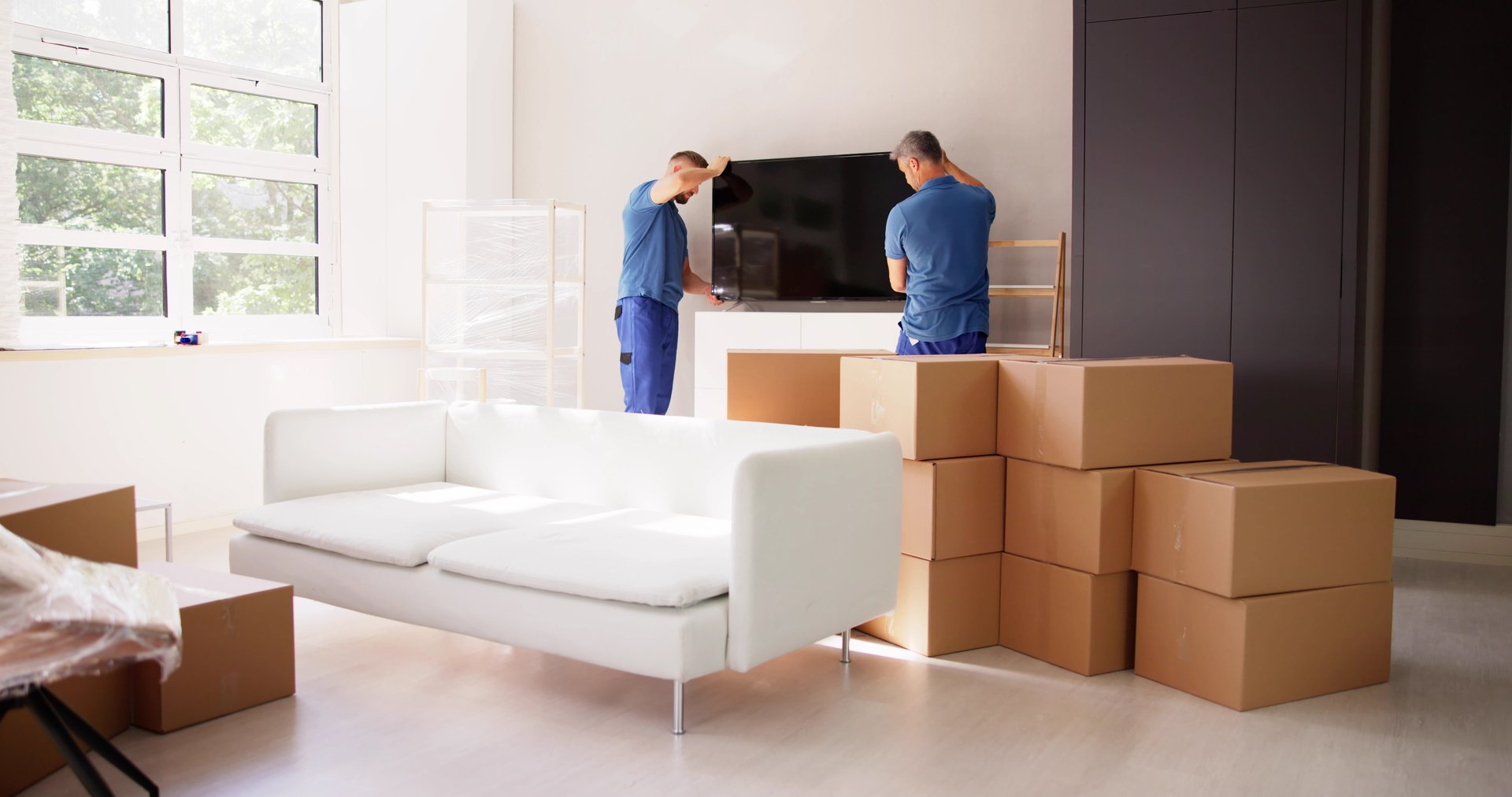 Two Young Male Movers In Uniform Placing Television In Living Room