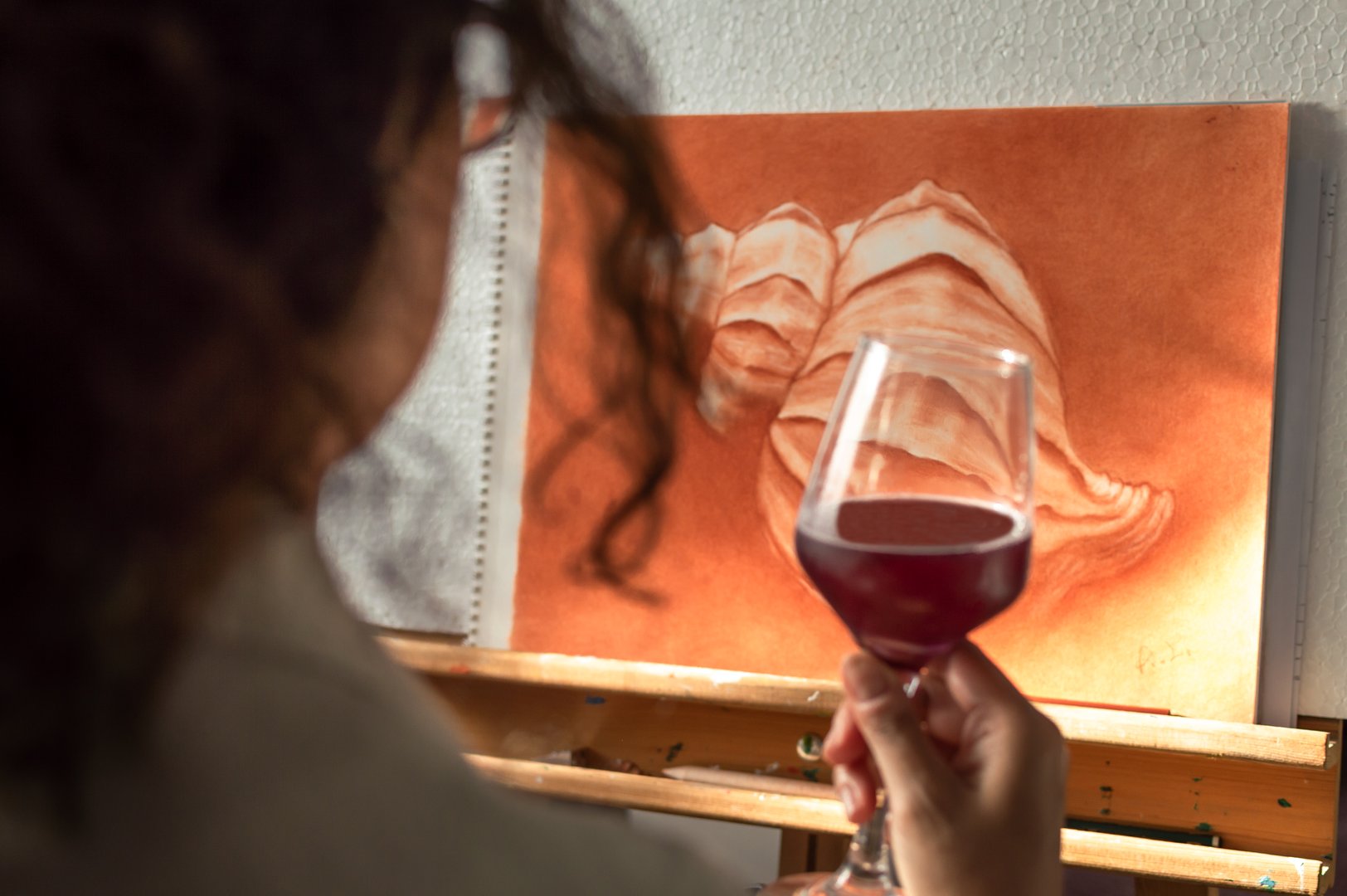 Woman drinking a glass of wine to celebrate that she has finished her painting.
