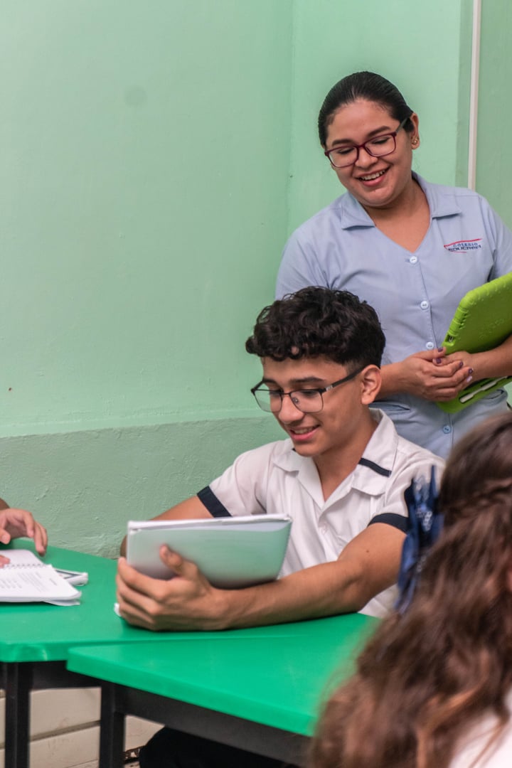 Estudiante con libreta y maestra con tablet
