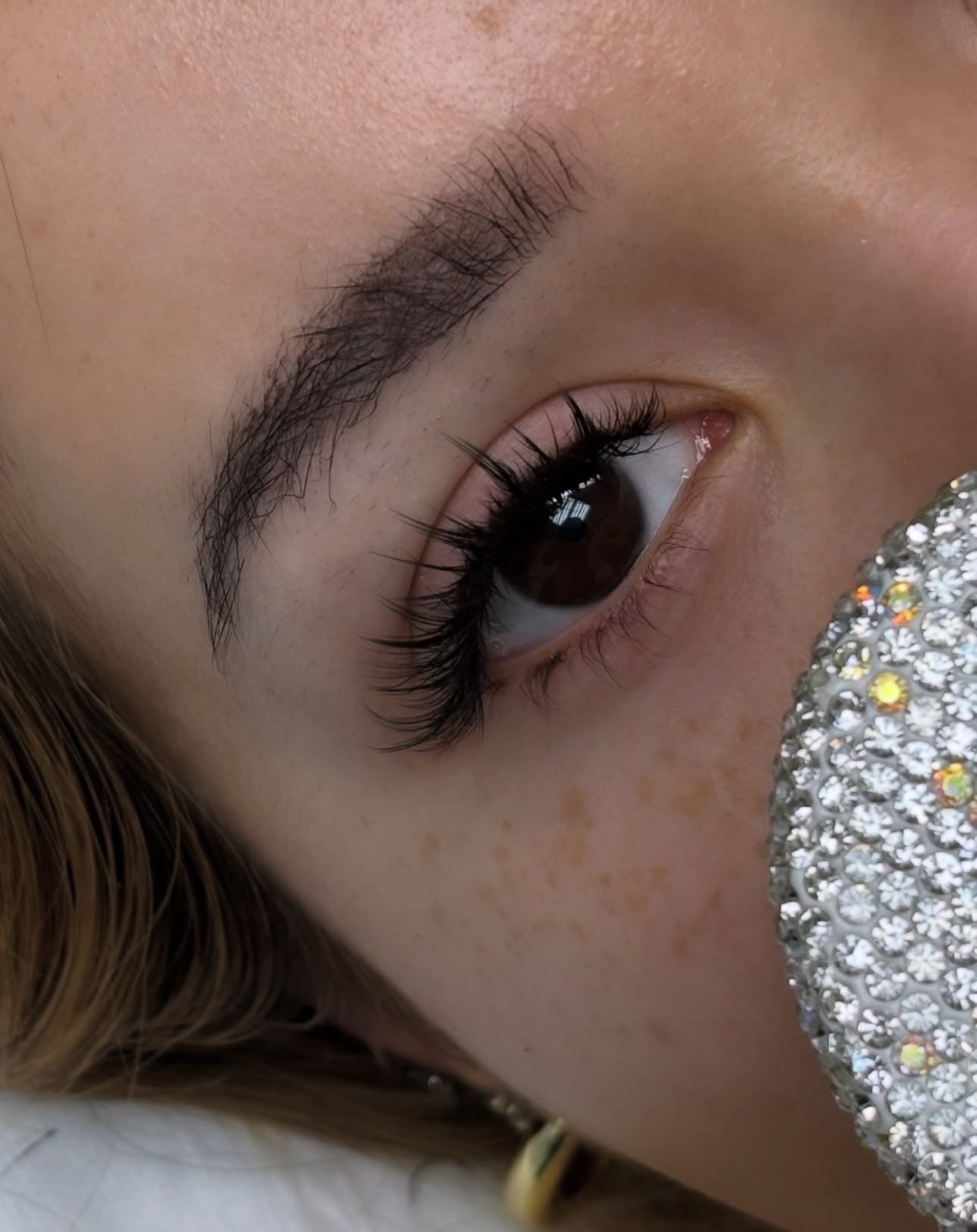 Close-up of a woman with dark hair and dramatic eye makeup, including long eyelashes and winged eyeliner, looking downward.