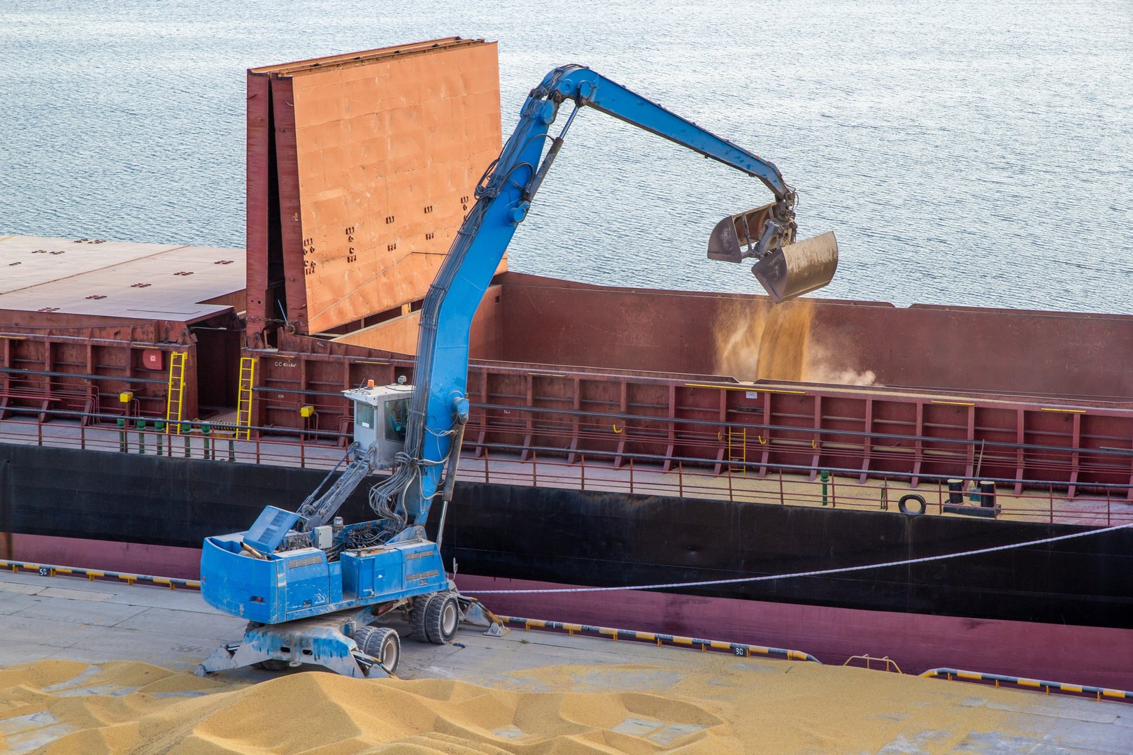 Unloading a dump truck with grain at the pier and reloading grain with a grab manipulator and a mobile conveyor into the ship's hold
