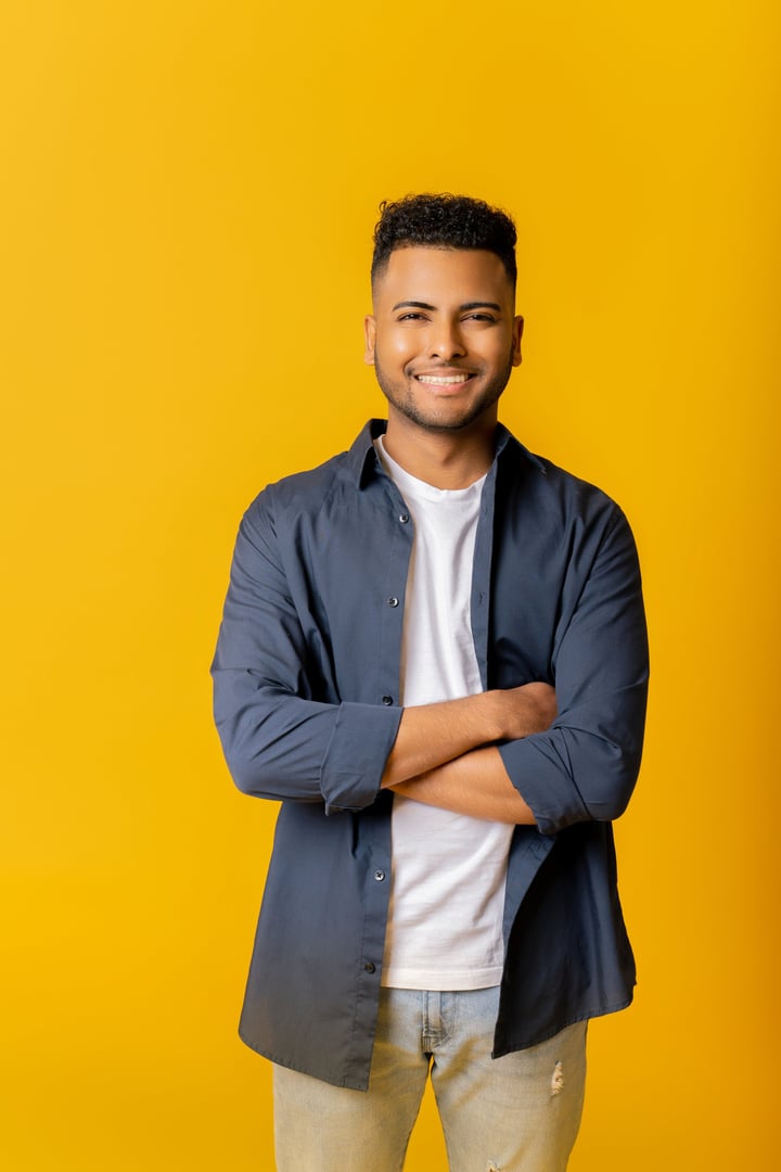Nice smiling indian male entrepreneur isolated on yellow, portrait of happy determined male student looking at camera with arms crossed, arab man posing in studio