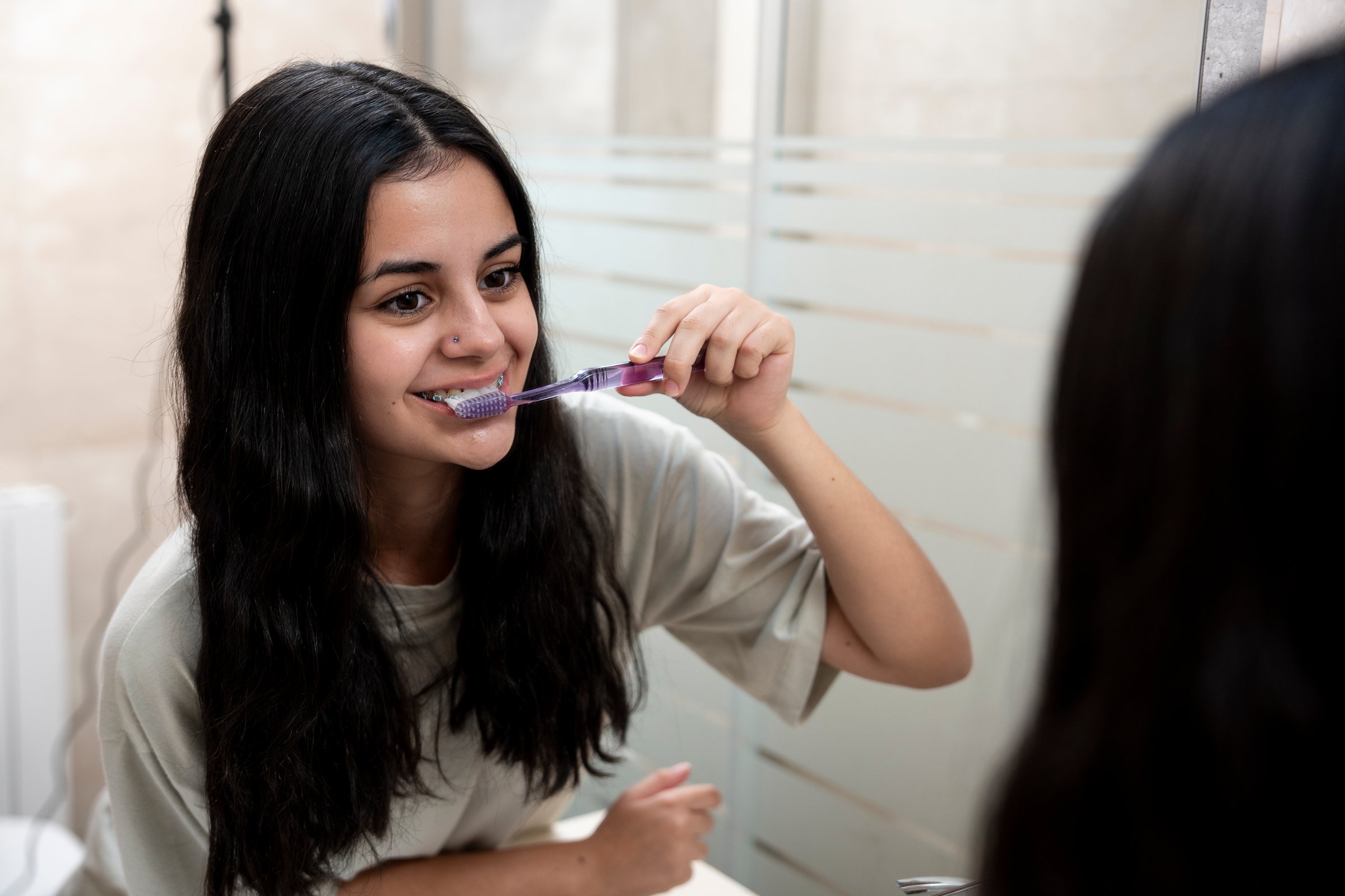 Teen brunette with braces brushing her teeth in front of the mirror