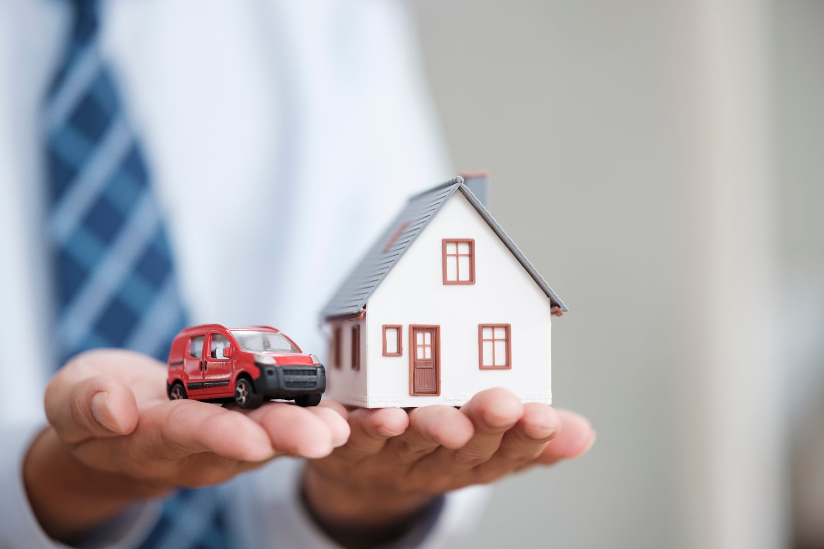 Hands holding car and house. Home loan, car insurance, family life assurance protection, financial mortgage for house building, and legacy planning investment concept.
