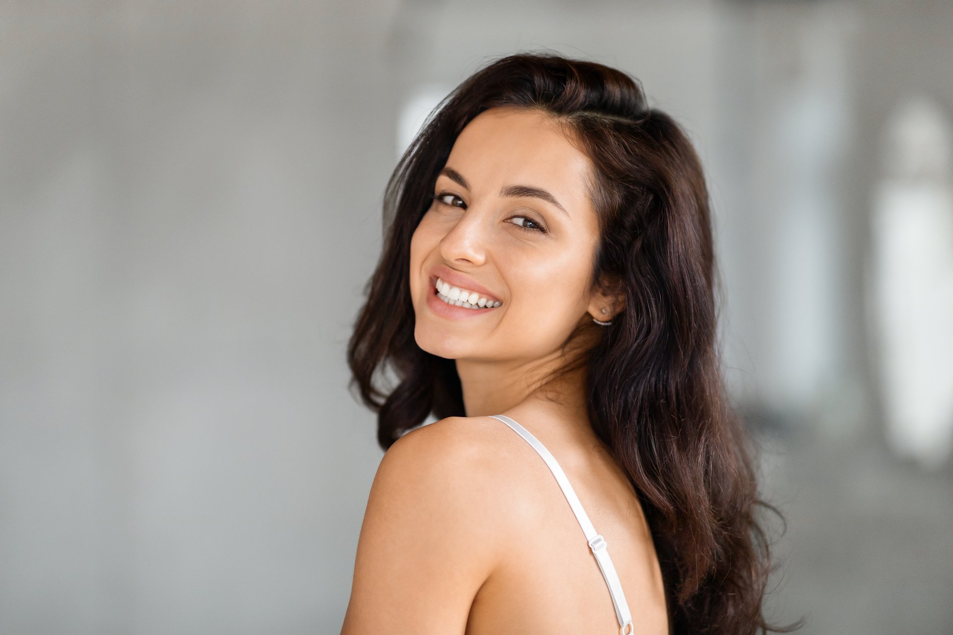 Portrait of attractive brunette long-haired millennial woman in underwear smiling at camera, copy space. Beautiful middle eastern lady enjoying body care at home, pampering concept