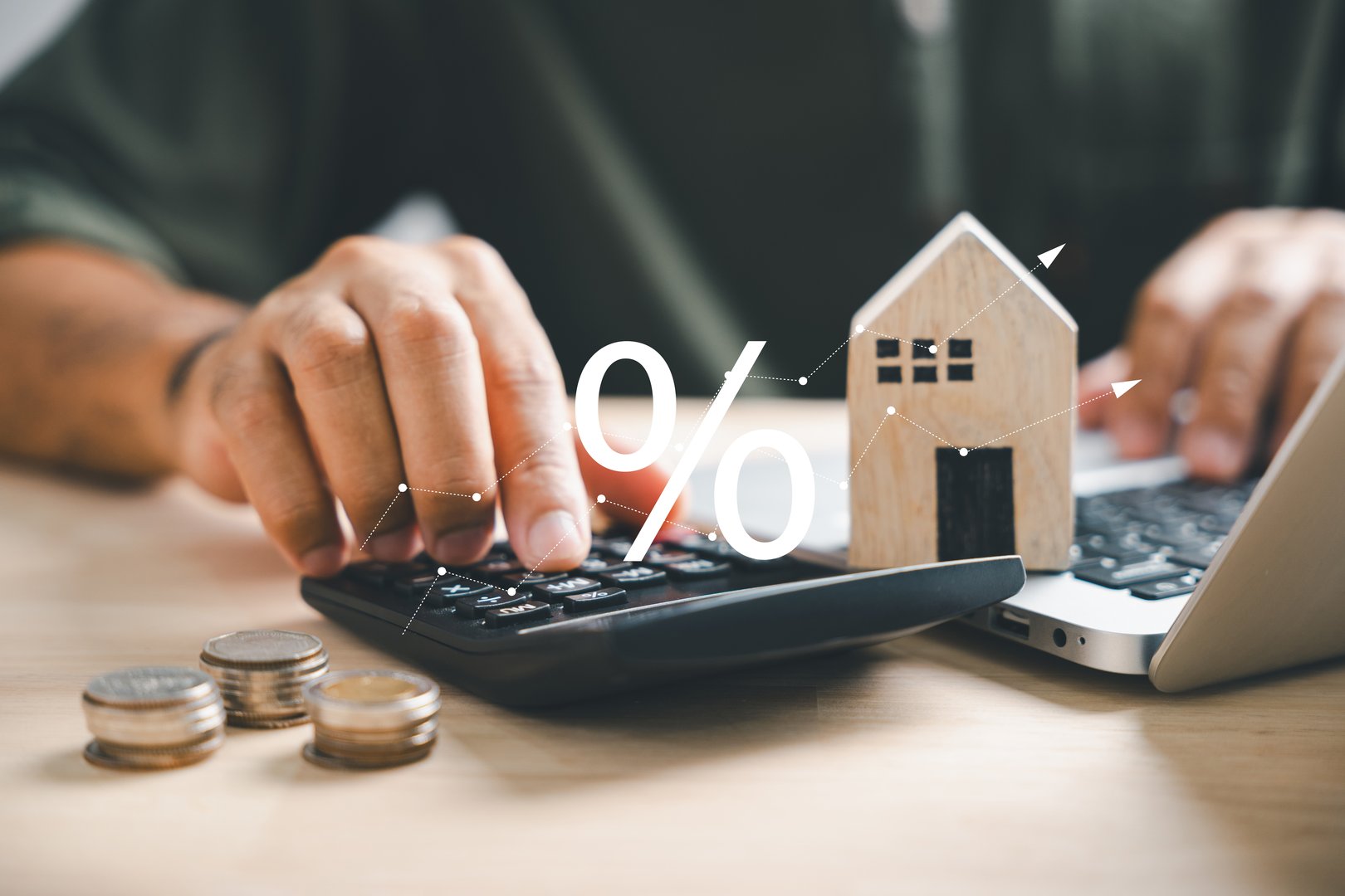 Hand on calculators, strategizing home refinance. Wooden house model, buy/rent note on desk. Smart money management for buying property concept. Tax, credit analysis for mortgage payment.