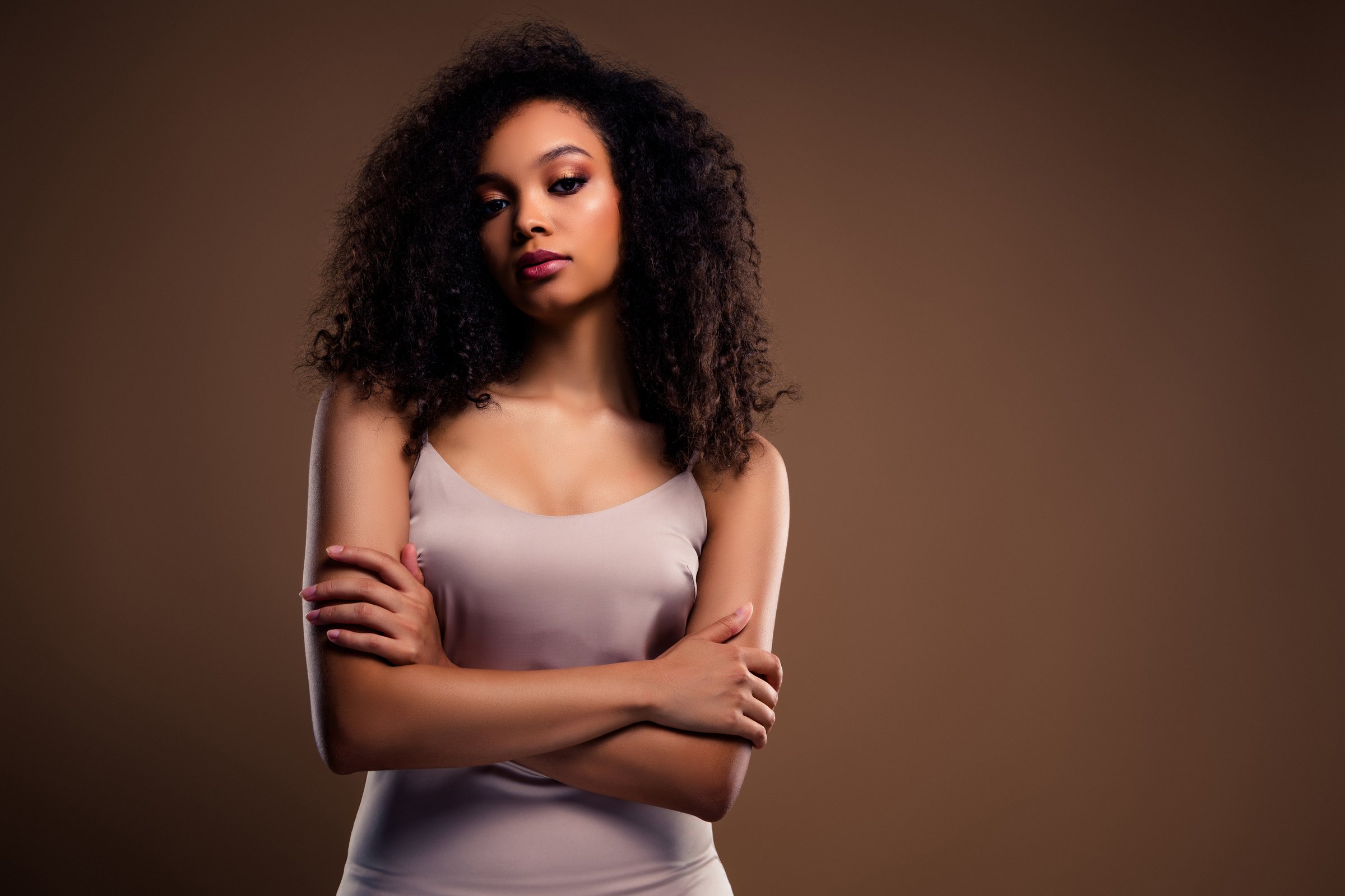 Stunning portrait of a fashionable young female model with curly hair and sophisticated style. The warm-toned background complements her graceful poise, highlighting beauty, elegance, and self-assurance.