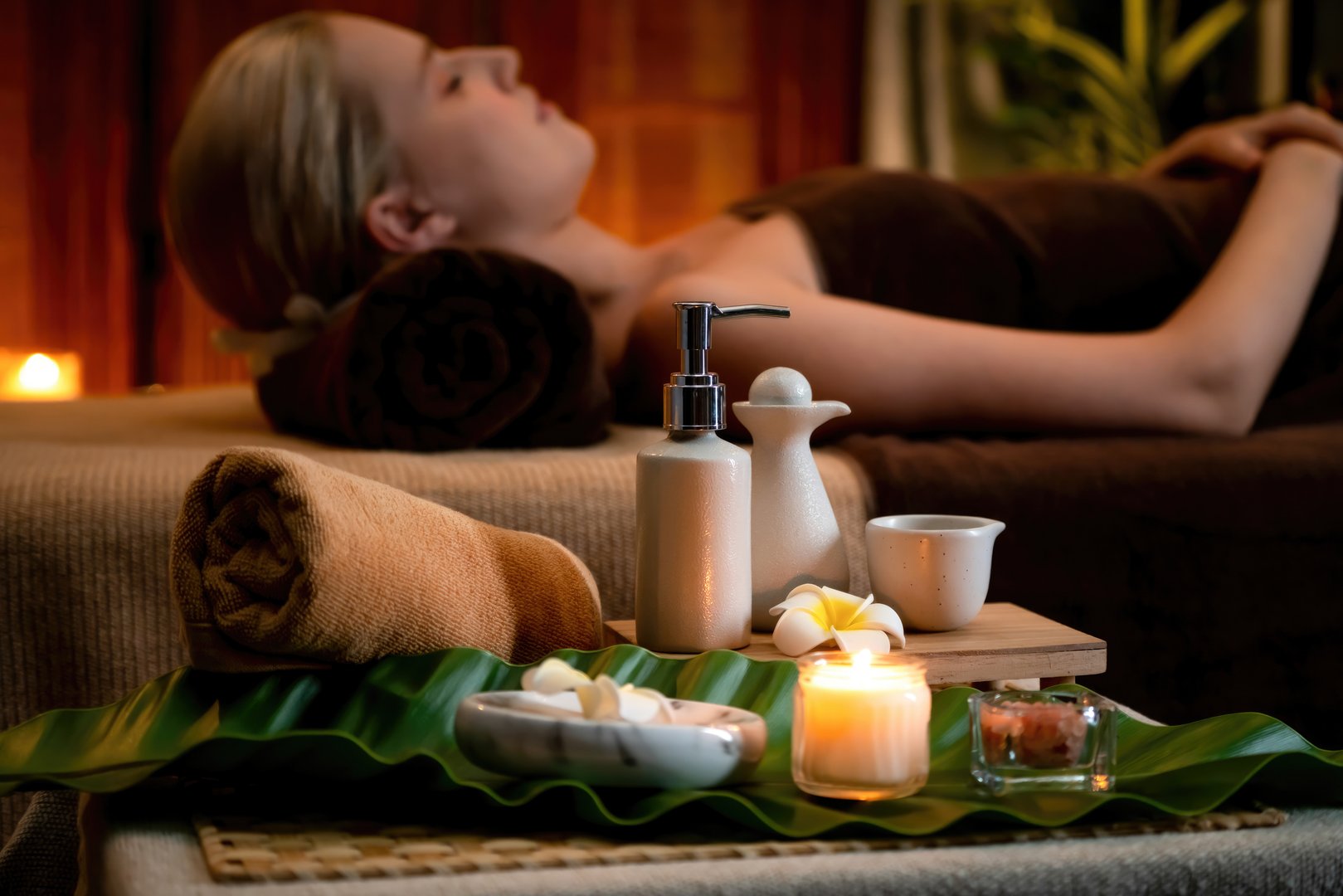 Aromatherapy massage ambiance or spa salon composition setup with focus decor candles and spa accessories on blurred woman enjoying blissful aroma spa massage in resort or hotel background. Quiescent