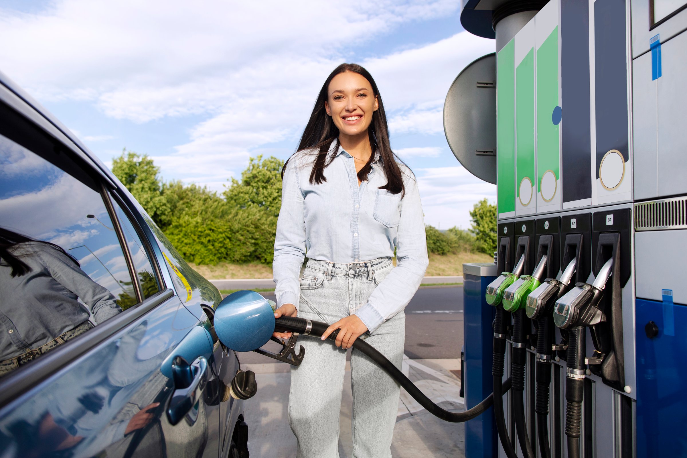 Eco friendly refueling concept. Happy European woman filling up her automobile with bio fuel at modern gas or petrol station, smiling at camera