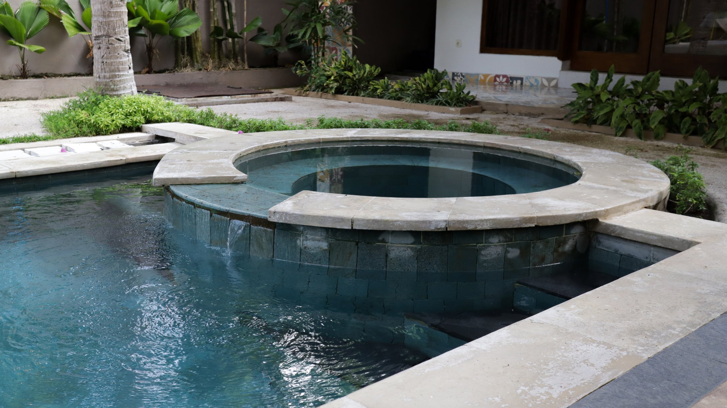 Luxury outdoor hot tub and swimming pool with serene blue tiles surrounded by lush garden greenery and modern villa elements in a tropical resort setting on a bright sunny day.