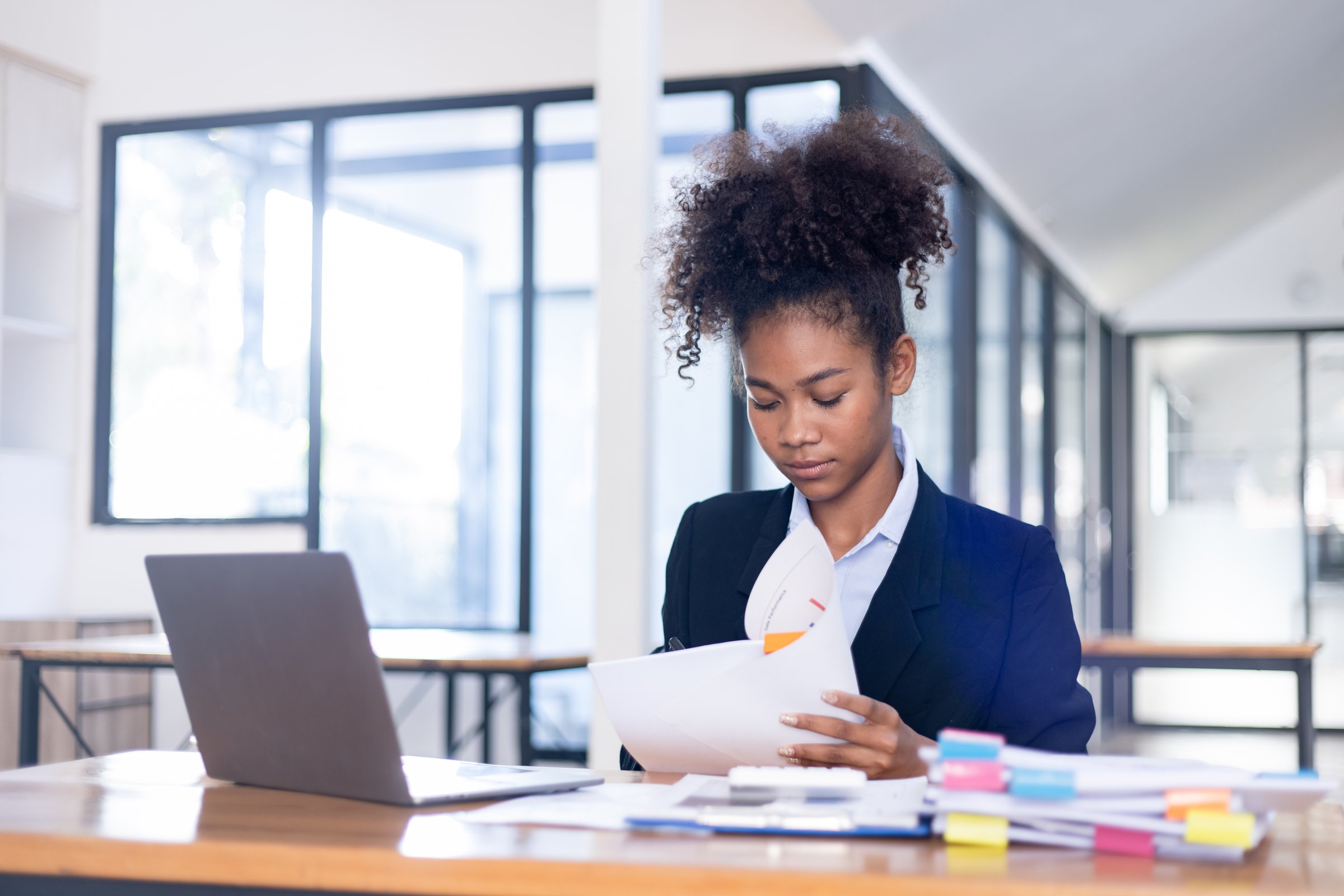 African American woman working laptop with paper documents on the desk in the office, Business planning and schedule of agenda in startup agency concept.
