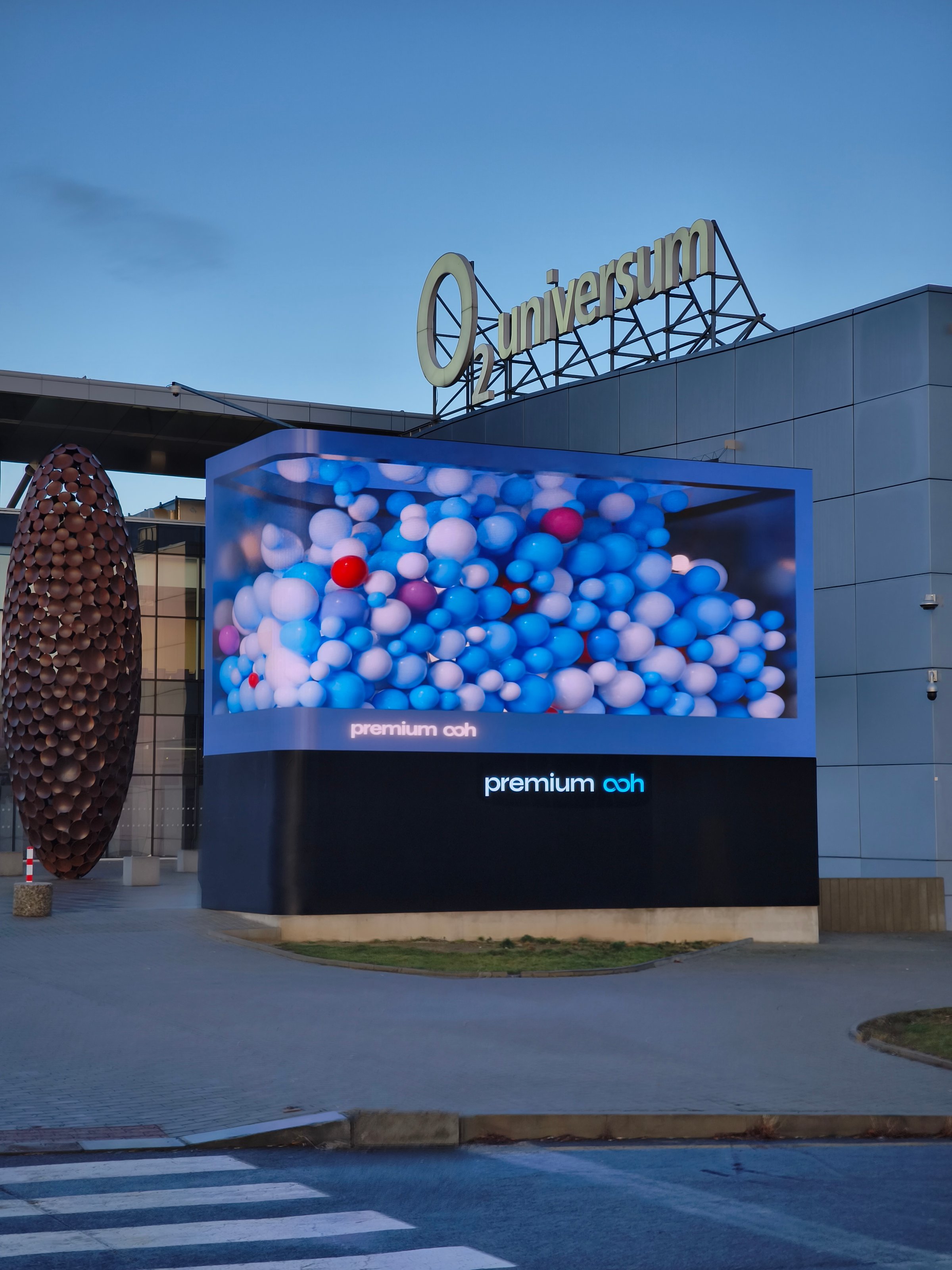 Colorful balloons fill an oversized glass container, creating a vibrant festive display outside the O2 Universum Conference Center in Prague, Czech Republic, on January 9, 2025. The installation is part of a premium OOH 3D billboard advertising campaign, adding a dynamic and eye-catching element to the urban landscape.
