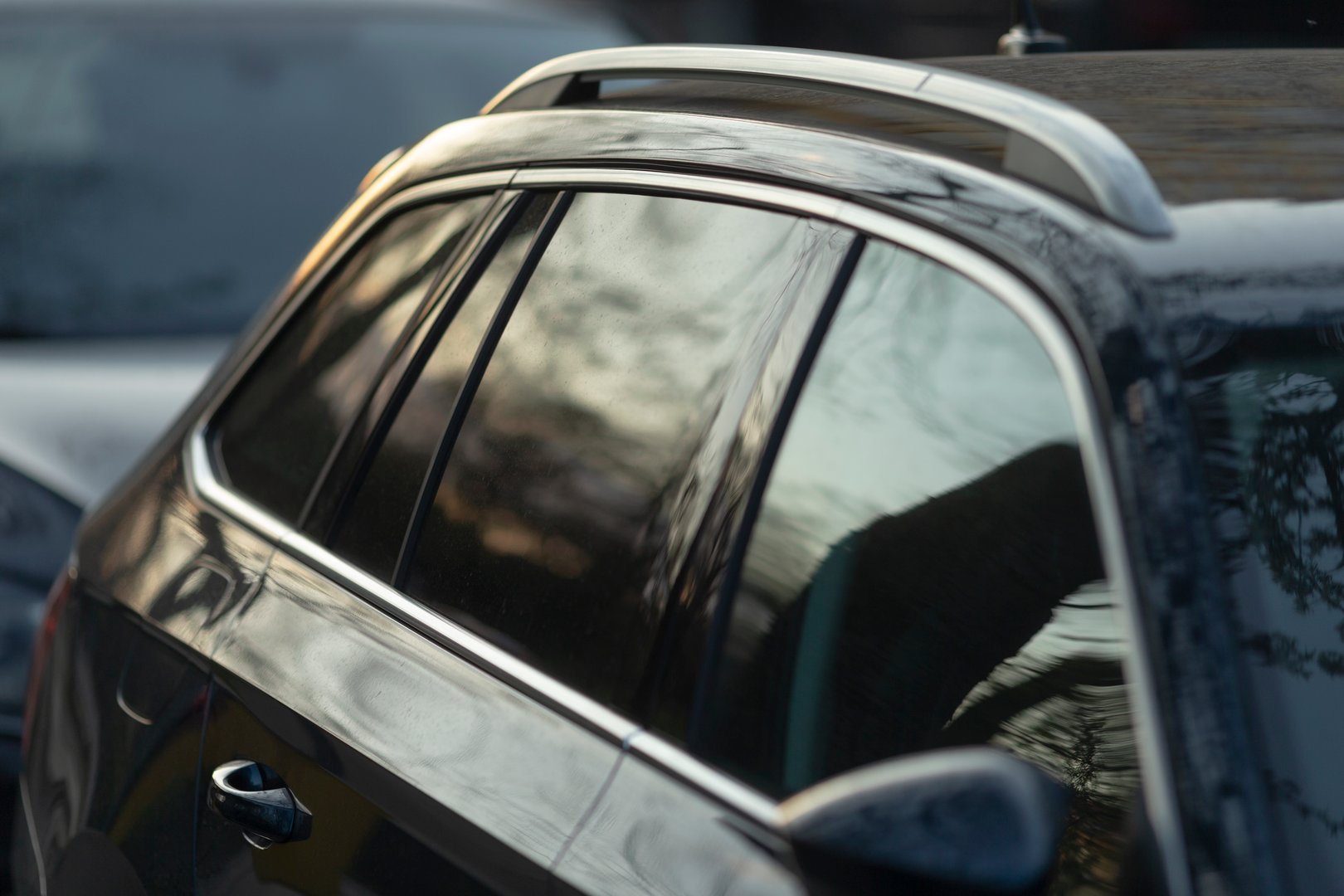 The image beautifully captures a detailed closeup of a cars roof rack, featuring reflective tinted windows that showcase and mirror the surrounding scenery and environment