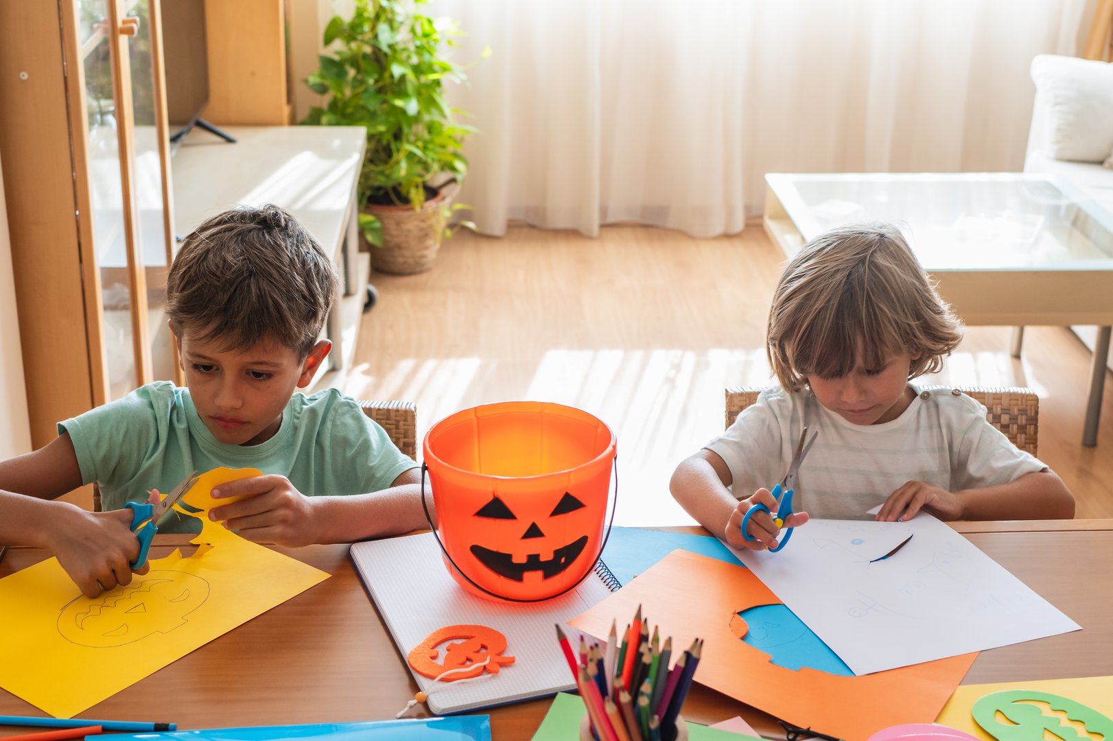 Two kids crafting Halloween decorations with scissors and colored paper.