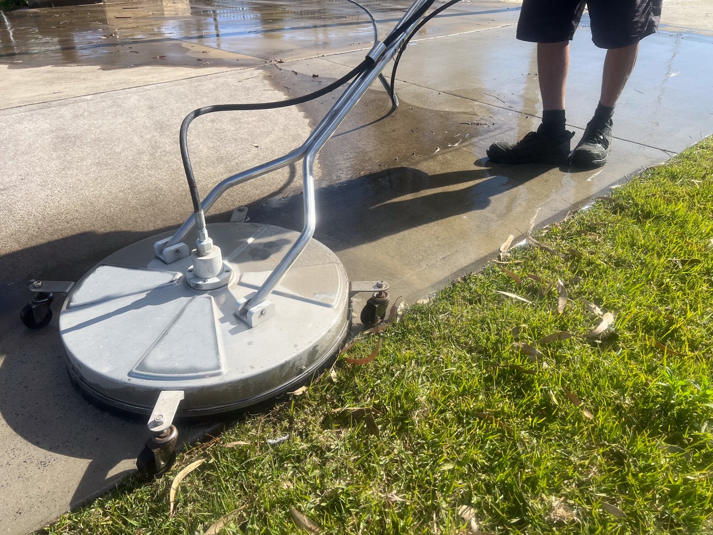 Worker using a floor and surface pressure washer cleaner high-pressure water spray to remove loose paint, mold, grime, dust, mud, and dirt from surfaces and objects.
