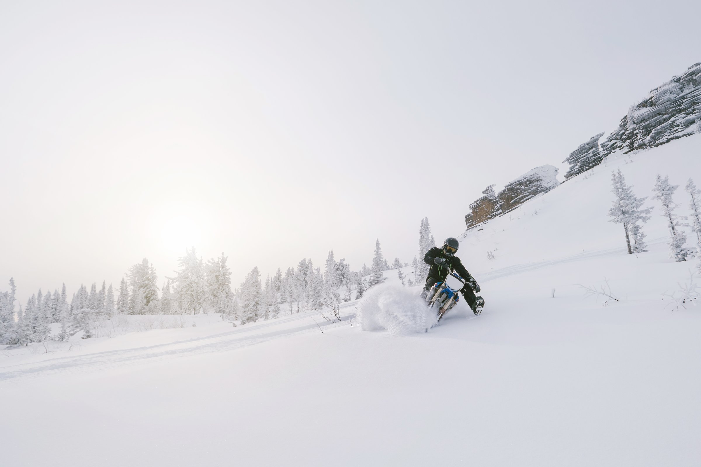 Rider with snowbike on snow covered mountain slop. Sunny fog, outdoor activity in winter day