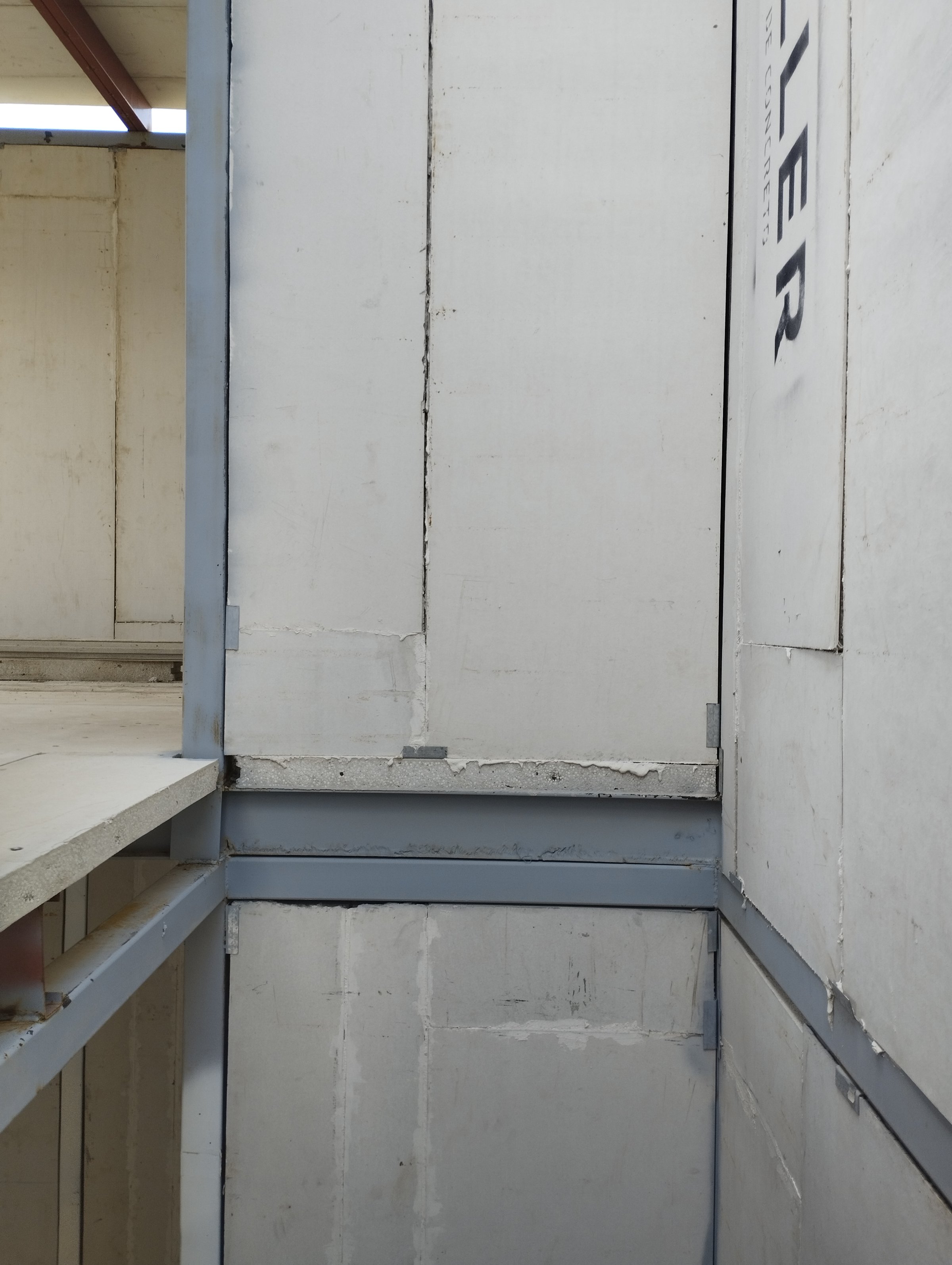 Interior view of an unfinished building with exposed metal beams and white insulation panels on the walls.