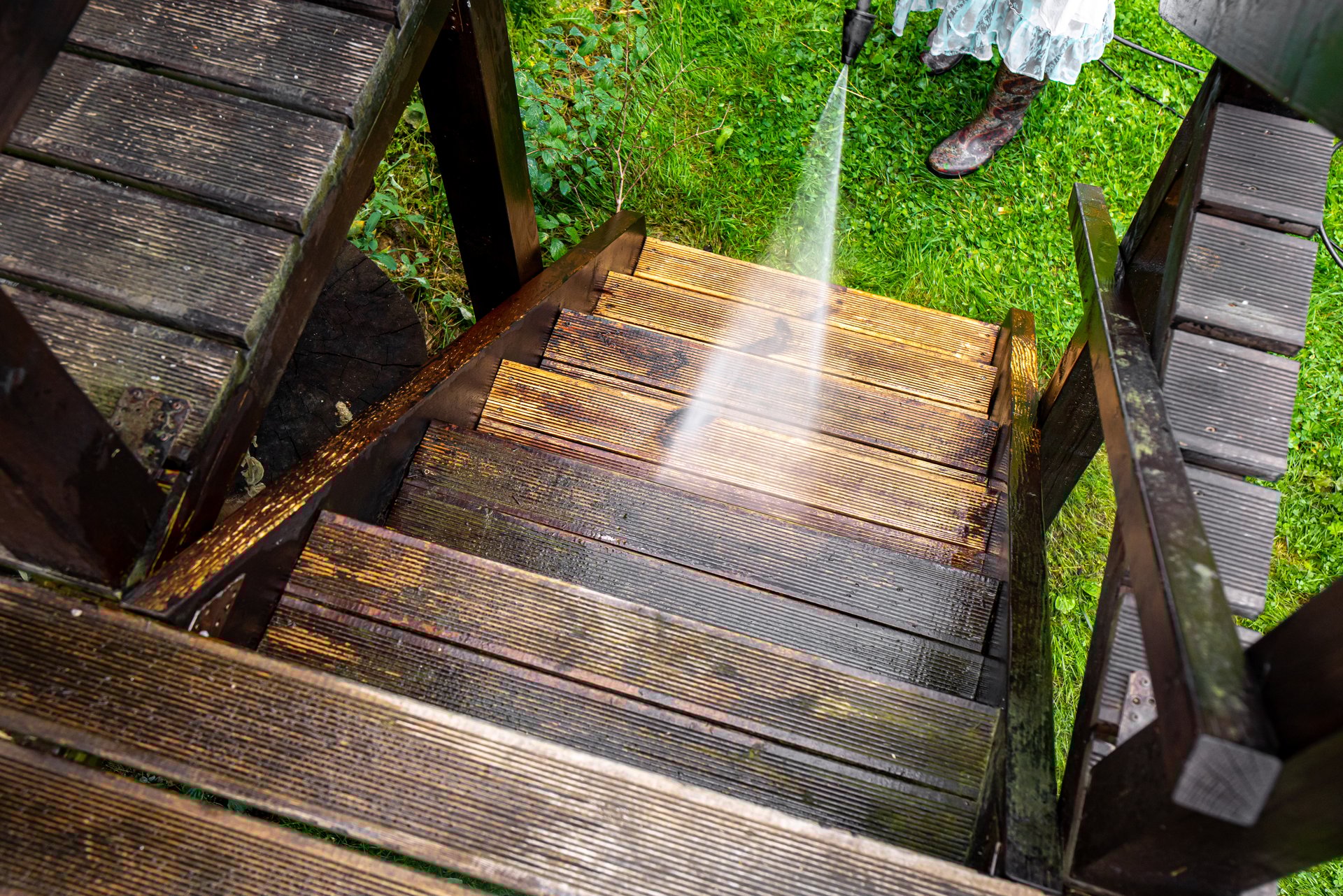 Close up view of using pressure washer to clean impregnated wood terrace stairs outdoors in the spring. Before cleaning and after, big contrast in color.
