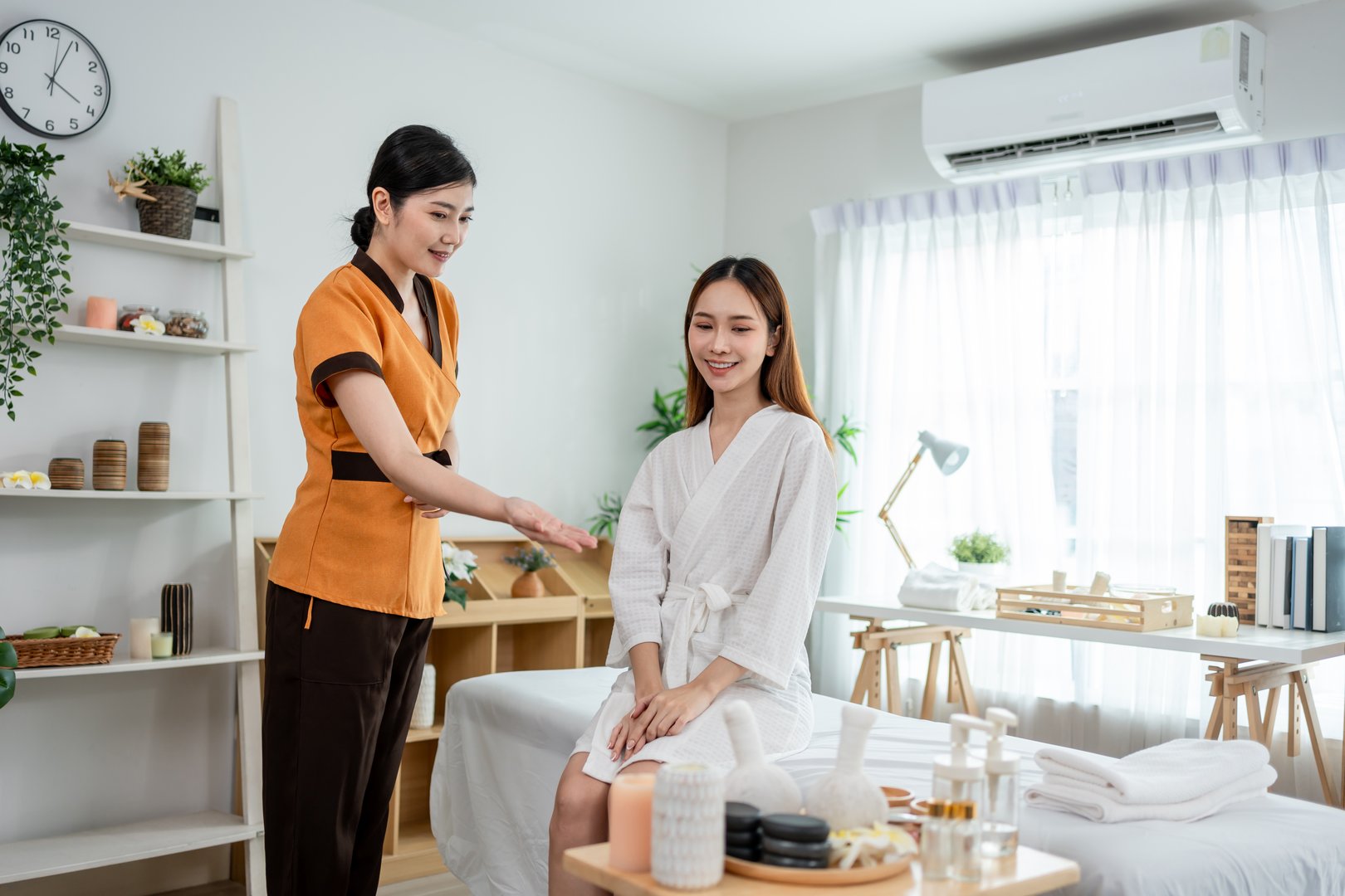 Asian female masseuse recommend spa treatment packages for customer. Attractive girl sitting on massage bed, feel happy and relax ready for physiotherapy treatment for body care in beauty spa clinic.