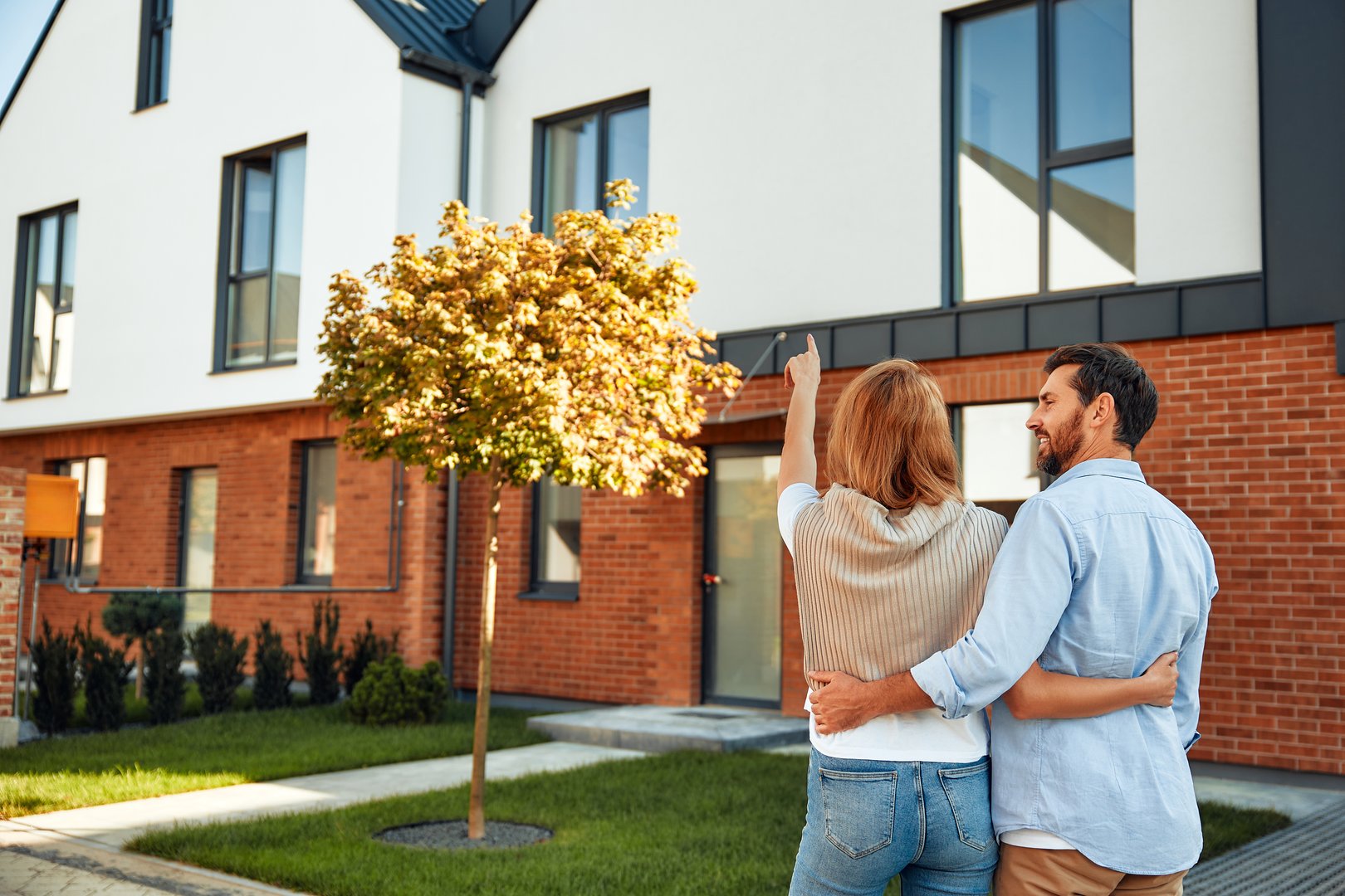 A young happiness married couple standing near a new house and hugging. Renting and buying a home. Moving concept.