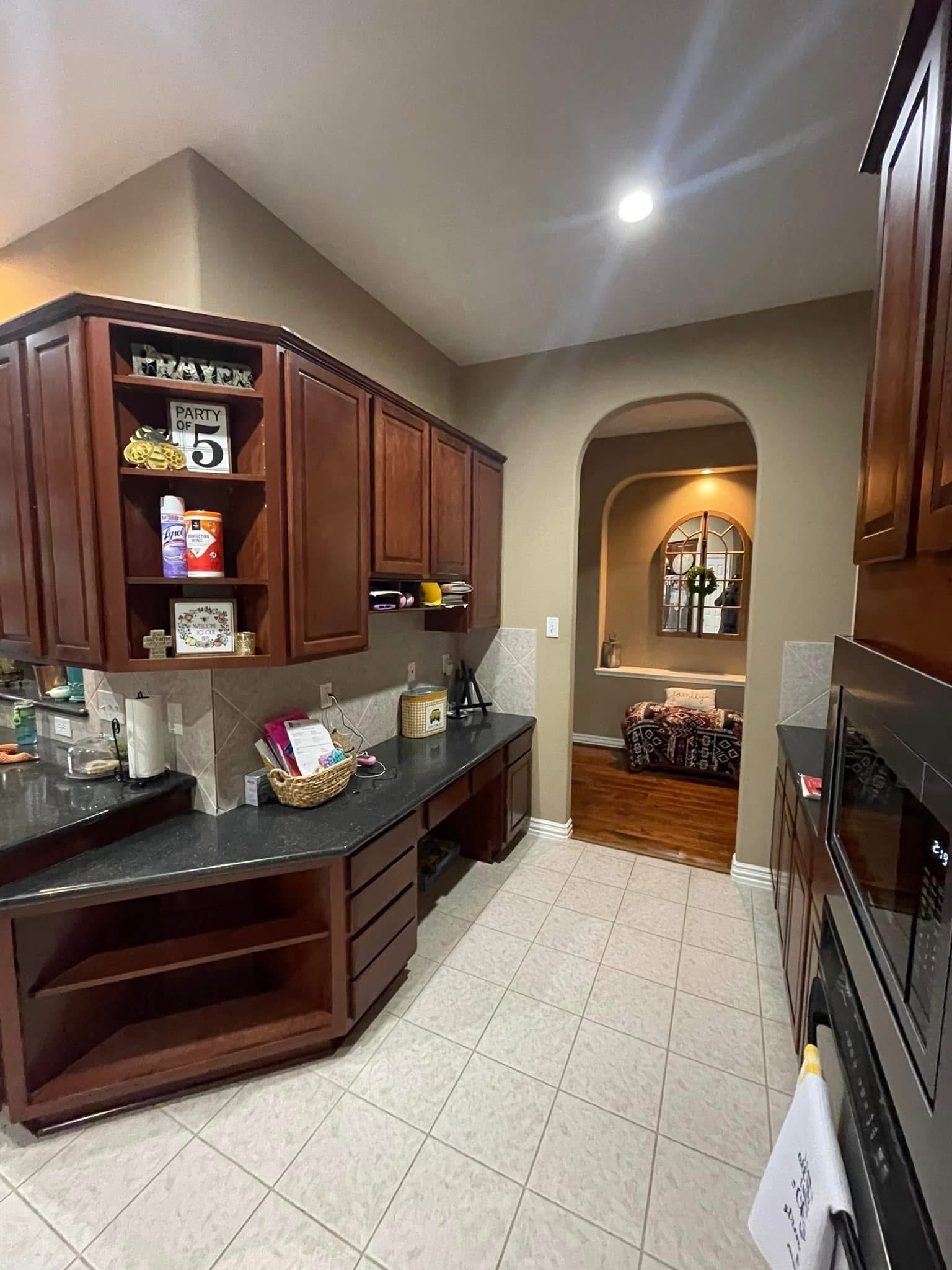 Spacious kitchen with dark wood cabinets, tiled floor, and a decorative archway leading to a warmly lit room.