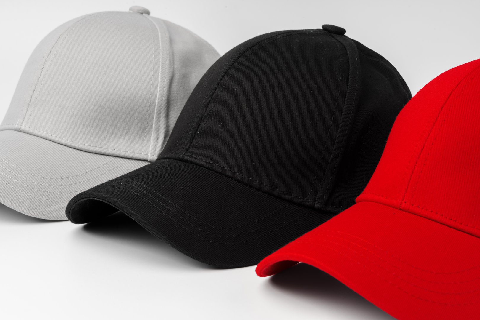 A selection of four baseball caps is neatly arranged in a row, showcasing the colors red, white, and black.