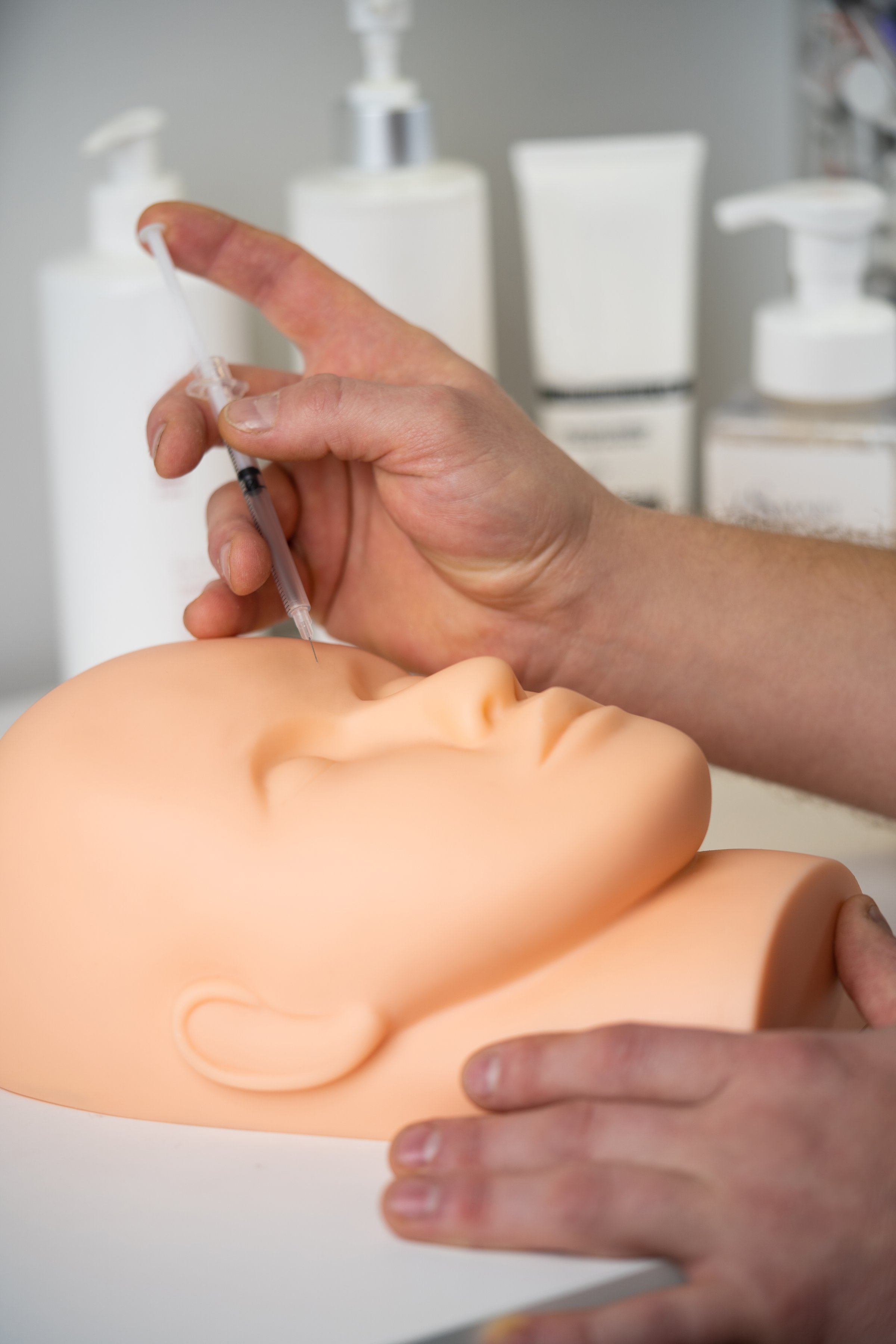 a cosmetologist trains to inject a cosmetic syringe into the face of a rubber mannequin