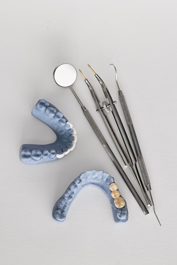 Dental mirror, tweezers, and explorer tool placed beside two dental casts: one with a bridge and another with veneers. Dental prosthetics and restorative treatment concept.