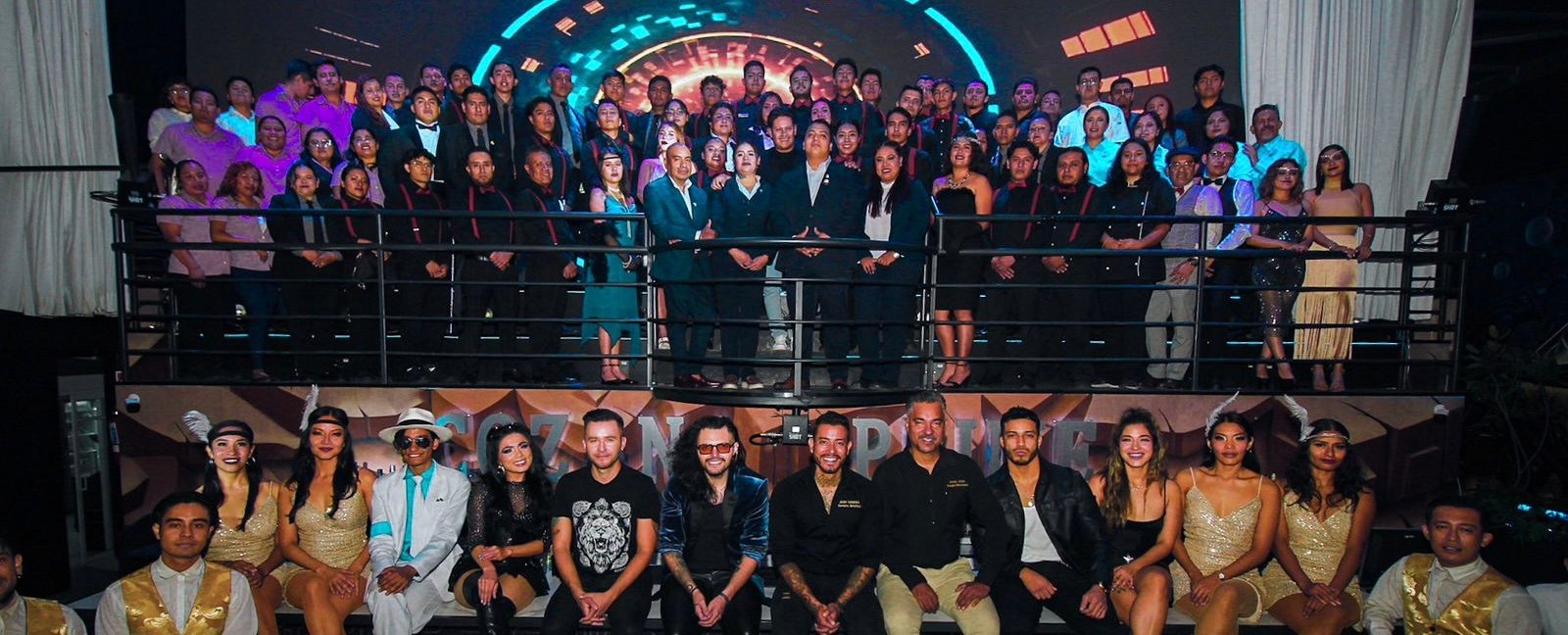 A large group posing at a formal event, with some in costumes. A mix of seated and standing individuals on a tiered stage.