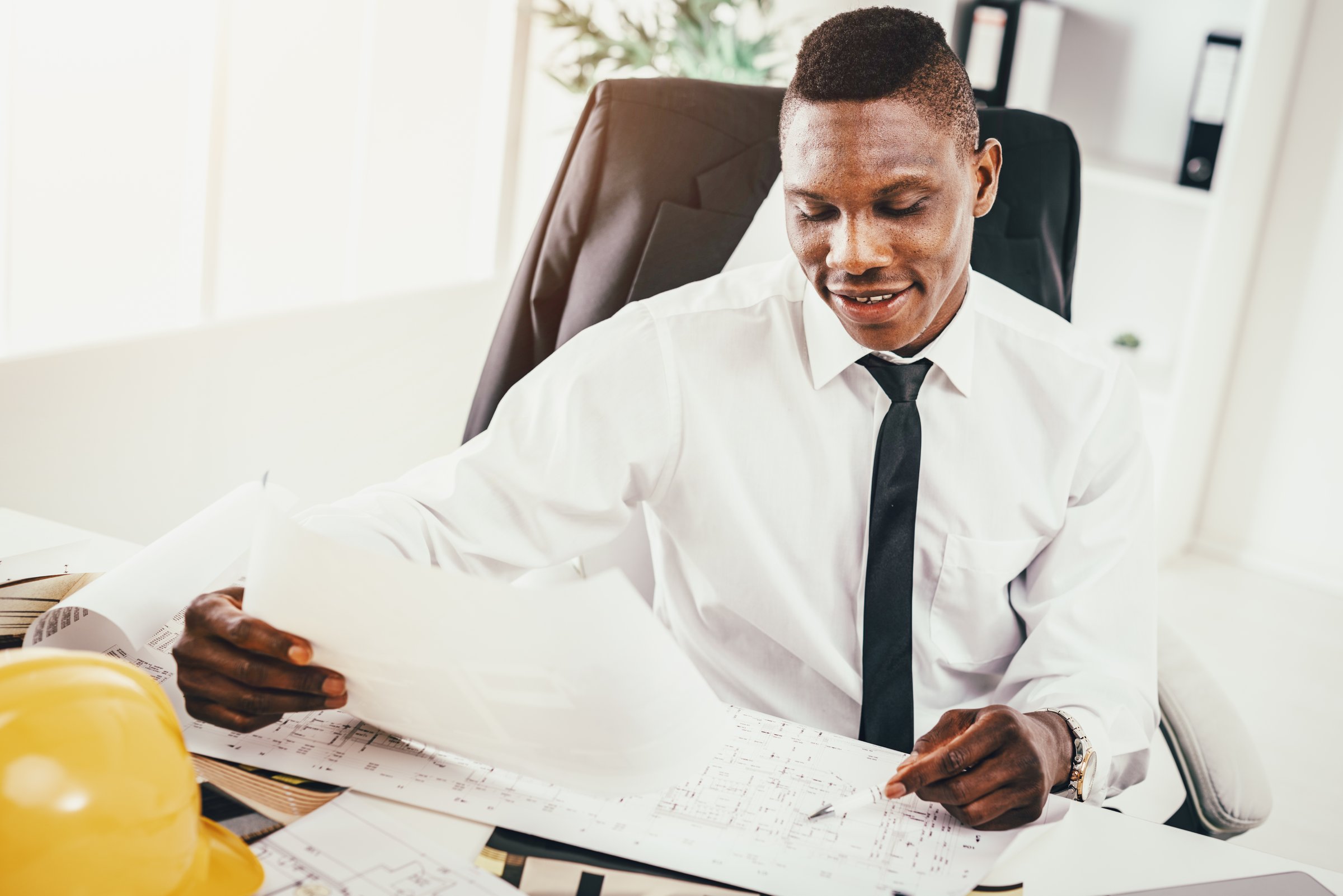 Succesful African architect analyzing blueprint in modern office and planning what to do next.