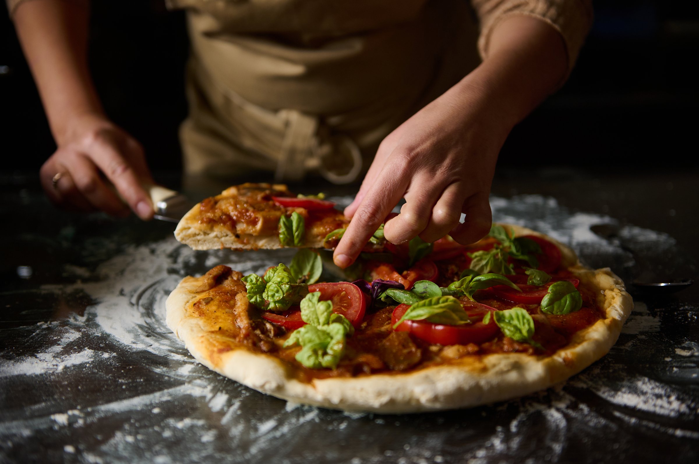 A chef slices a freshly baked pizza adorned with vibrant basil and tomatoes. The culinary scene is inviting, showcasing a delicious homemade touch.