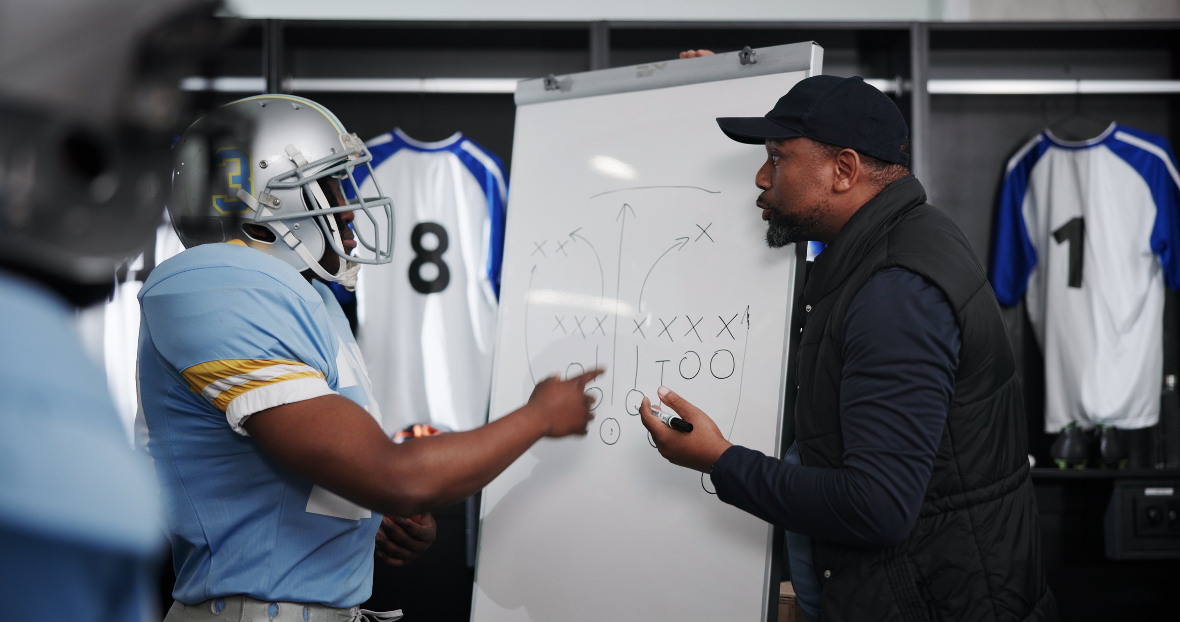 Board, writing and football with coach and team in locker room for game plan, sports strategy or defense formation. Touchdown tactics, match feedback and discussion with people and training advice
