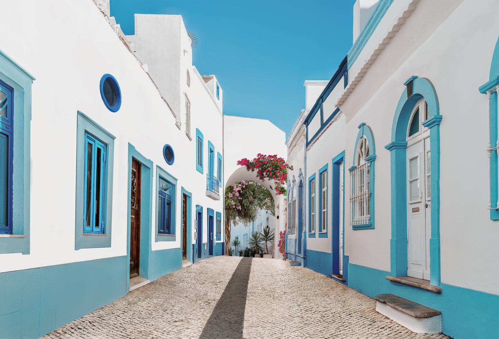 Street in fishing village with white and blue houses and typical Portuguese pavement in Olhao, Algarve region - Popular travel destinations in Portugal