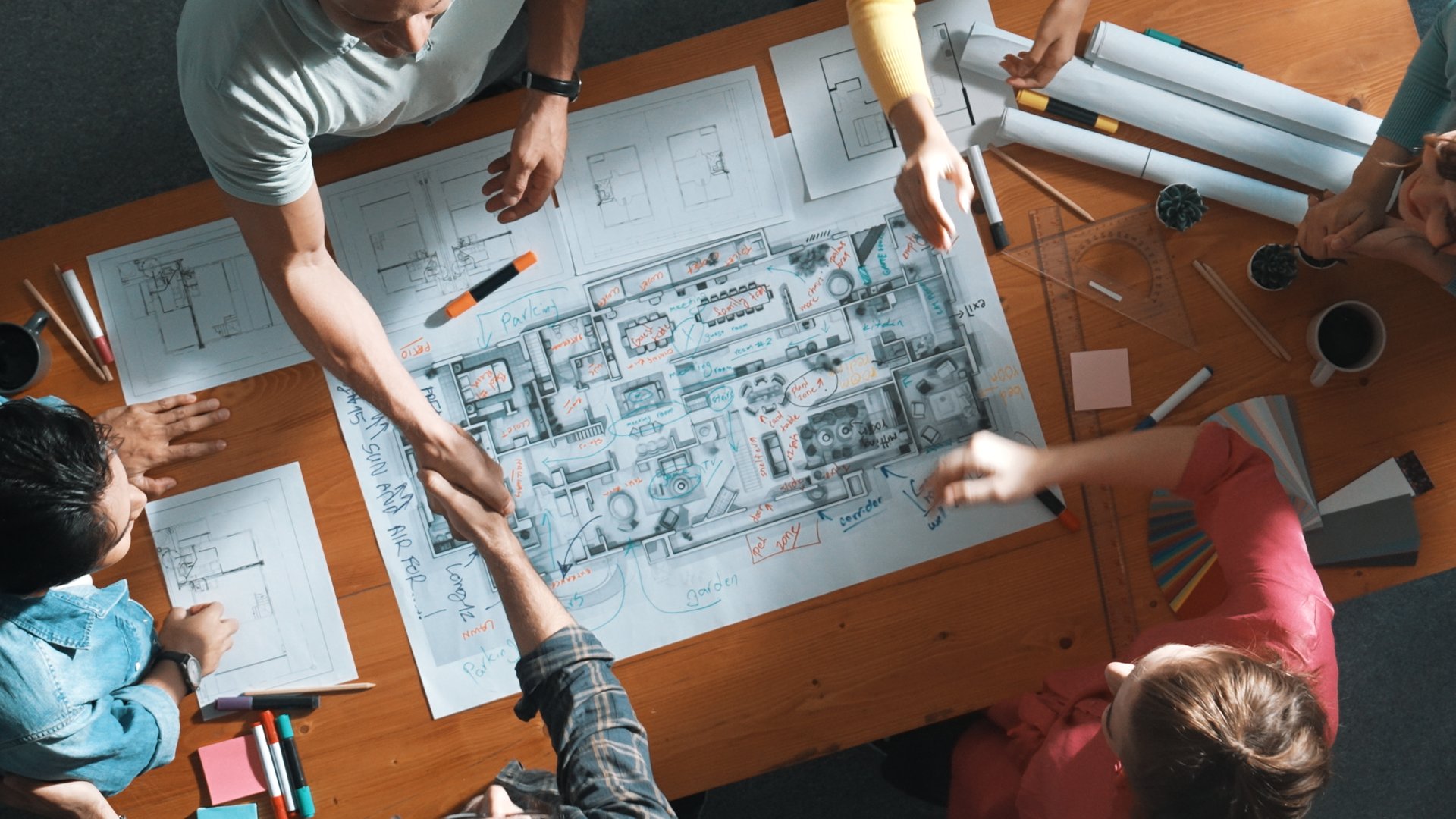 Top down view of smart business people shaking hands and making a contract. Aerial view of architect engineer working together and dealing plan or project at table with blueprint and notes. Symposium.