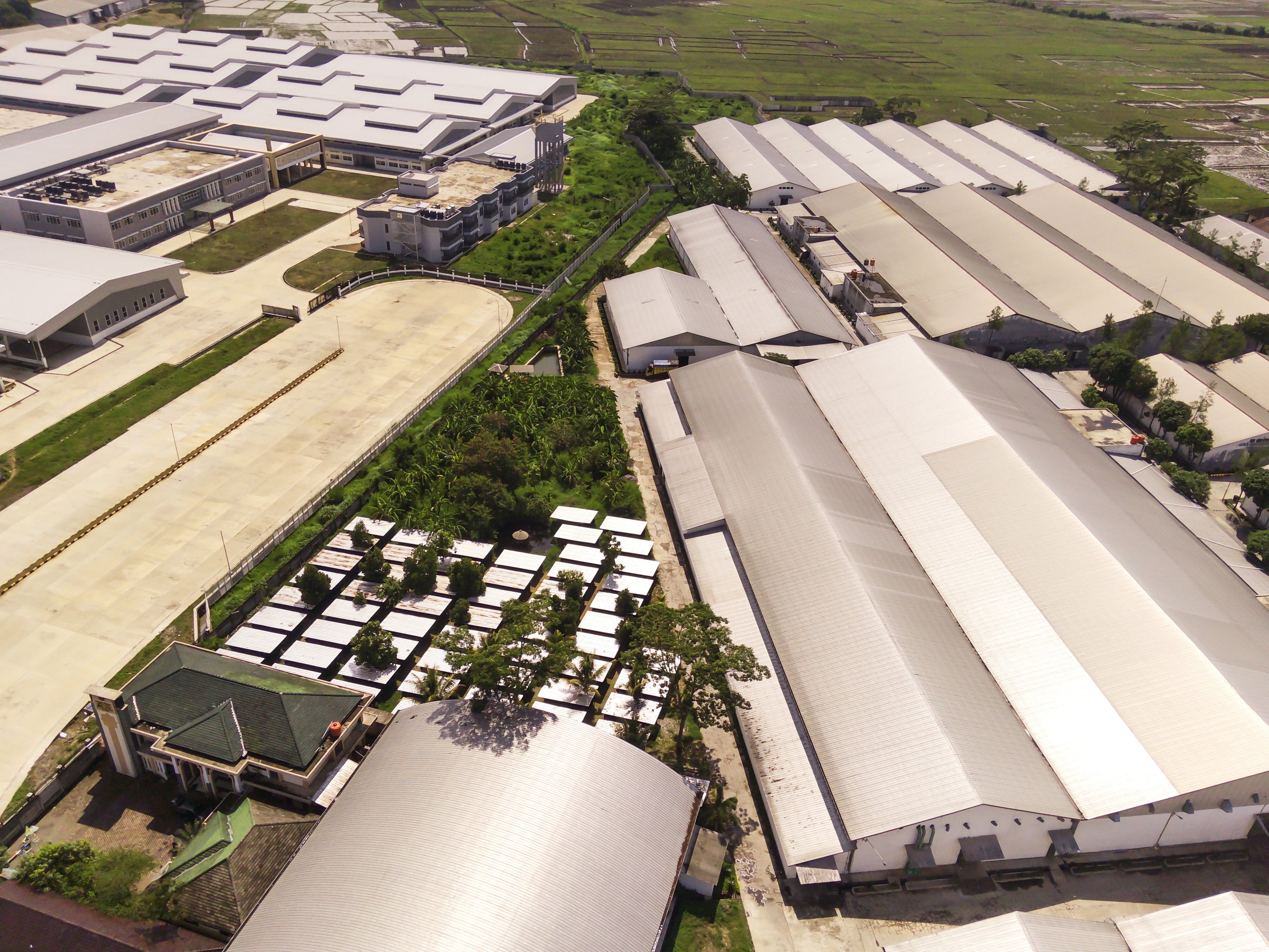 Large suburban industrial and logistic warehouse - aerial view at sunny day. Industrial District. Business and Economy. Factory buildings and warehouses around Majalaya area, West Java. Indonesia