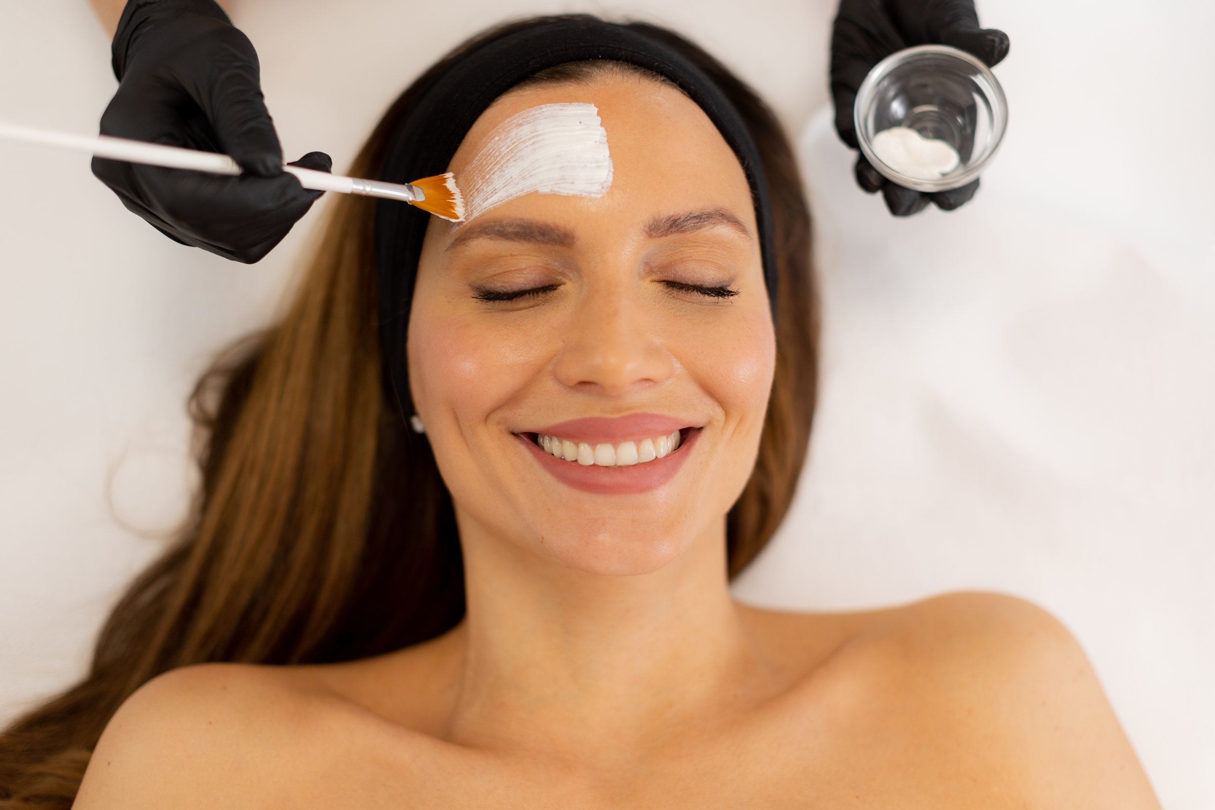 A patient enjoys a skin treatment as a skilled professional applies a soothing mask, surrounded by calming decor, in a tranquil wellness center atmosphere.