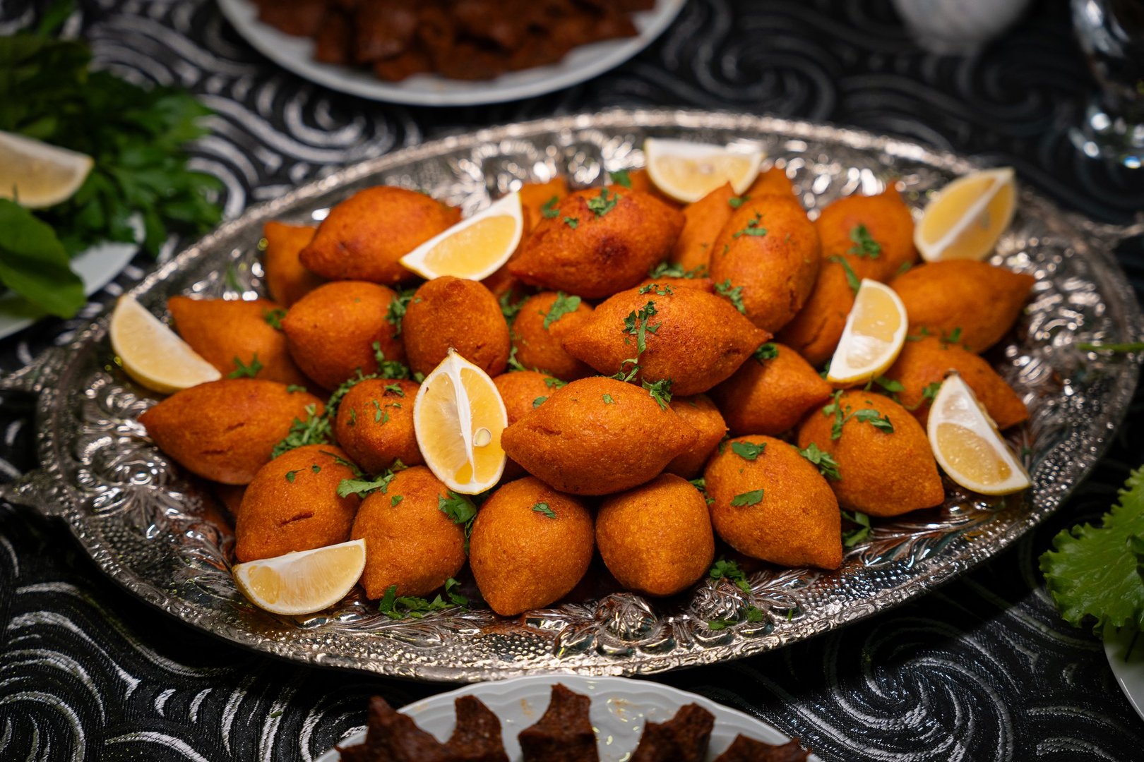 Golden fried stuffed bulgur meatballs, known as icli kofte or kibbeh, are a popular and delicious dish in both Turkish and Middle Eastern cuisine. These traditional appetizers are expertly served with fresh lemon wedges on an elegant silver tray, making for a sophisticated dinner concept.