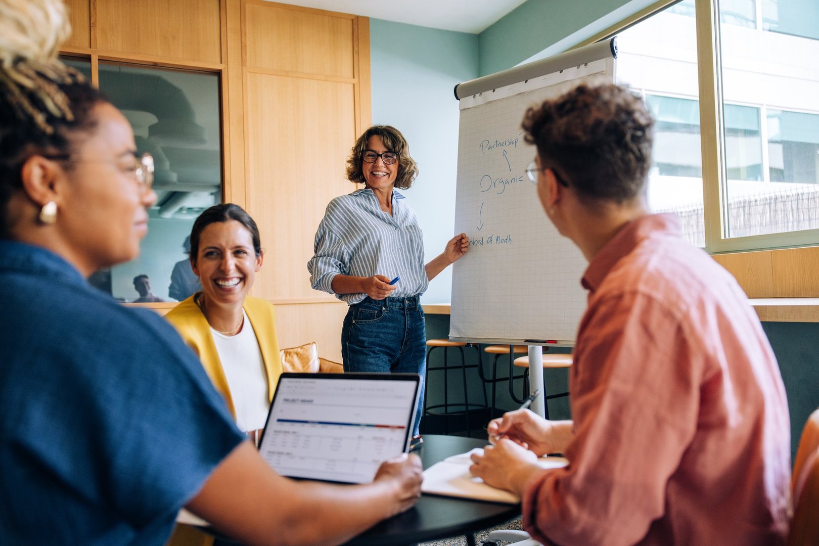A diverse team gathered in a meeting, discussing strategies with a visual aid. They appear engaged and dynamic, working collaboratively around a table surrounded by professional business tools.