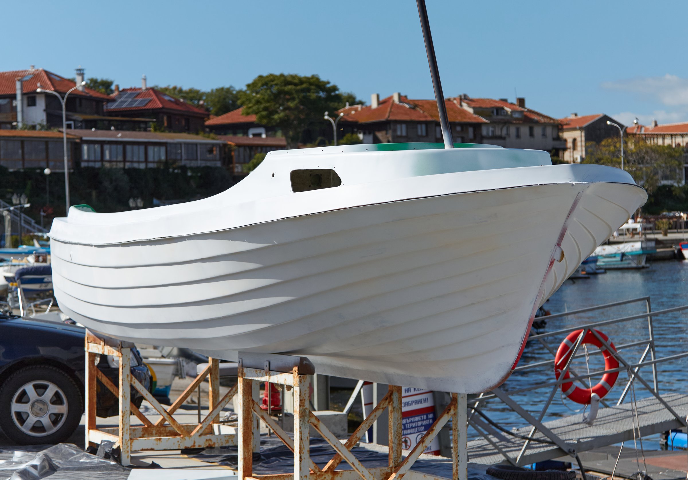 White boat on wooden supports at marina, surrounded by water and moored vessels, highlighting craftsmanship and marine environment with vibrant buildings nearby