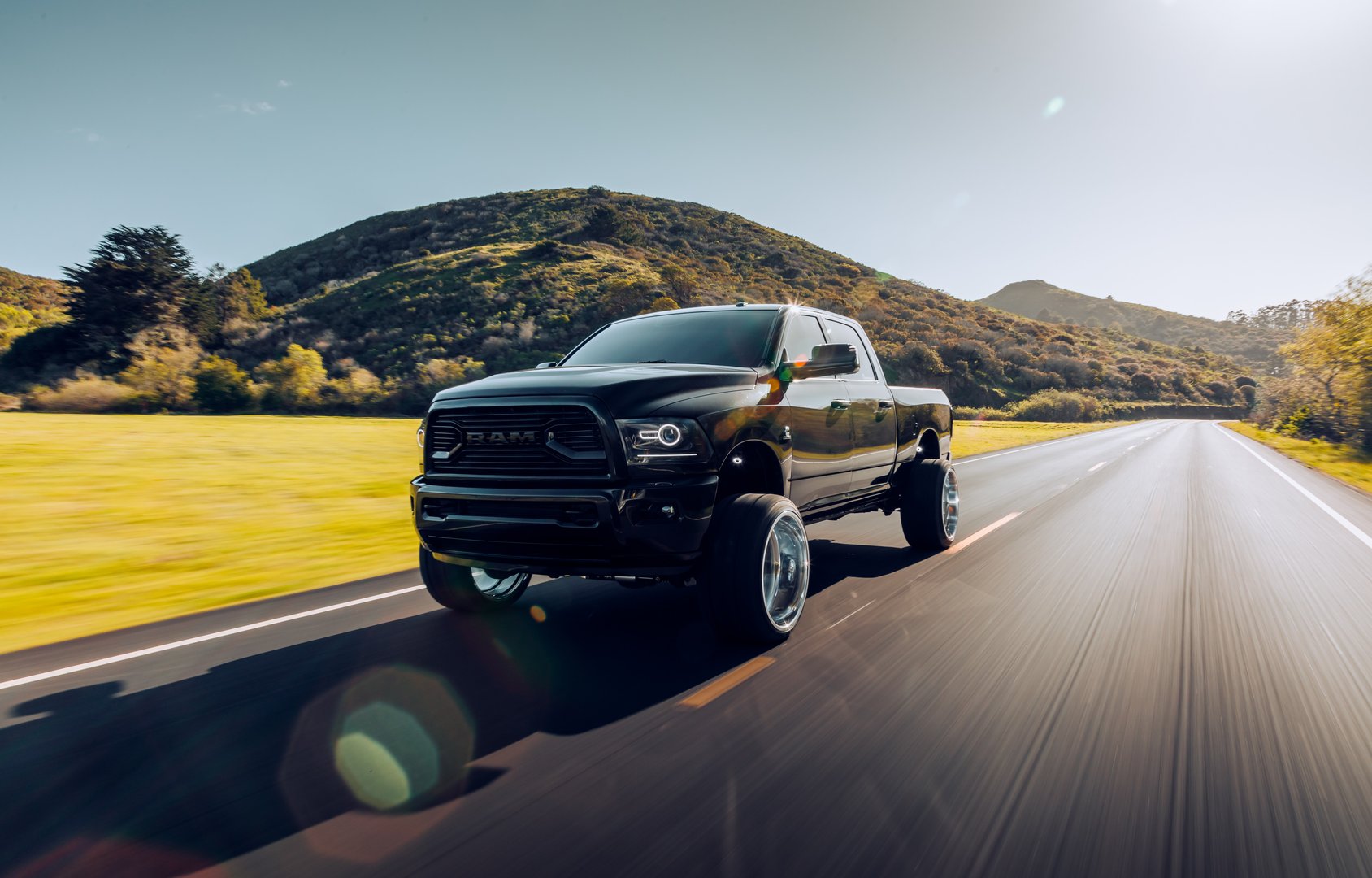 San Fran, CA, USA
5/1/2022
Lifted Black Dodge Ram Truck with larger wheels driving on a back road by itself