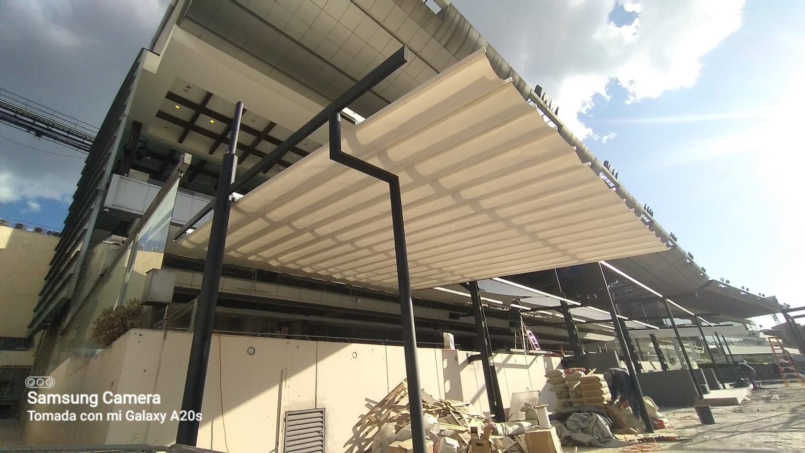 Construction site with a large awning being installed outside a modern building. Sky partially cloudy.