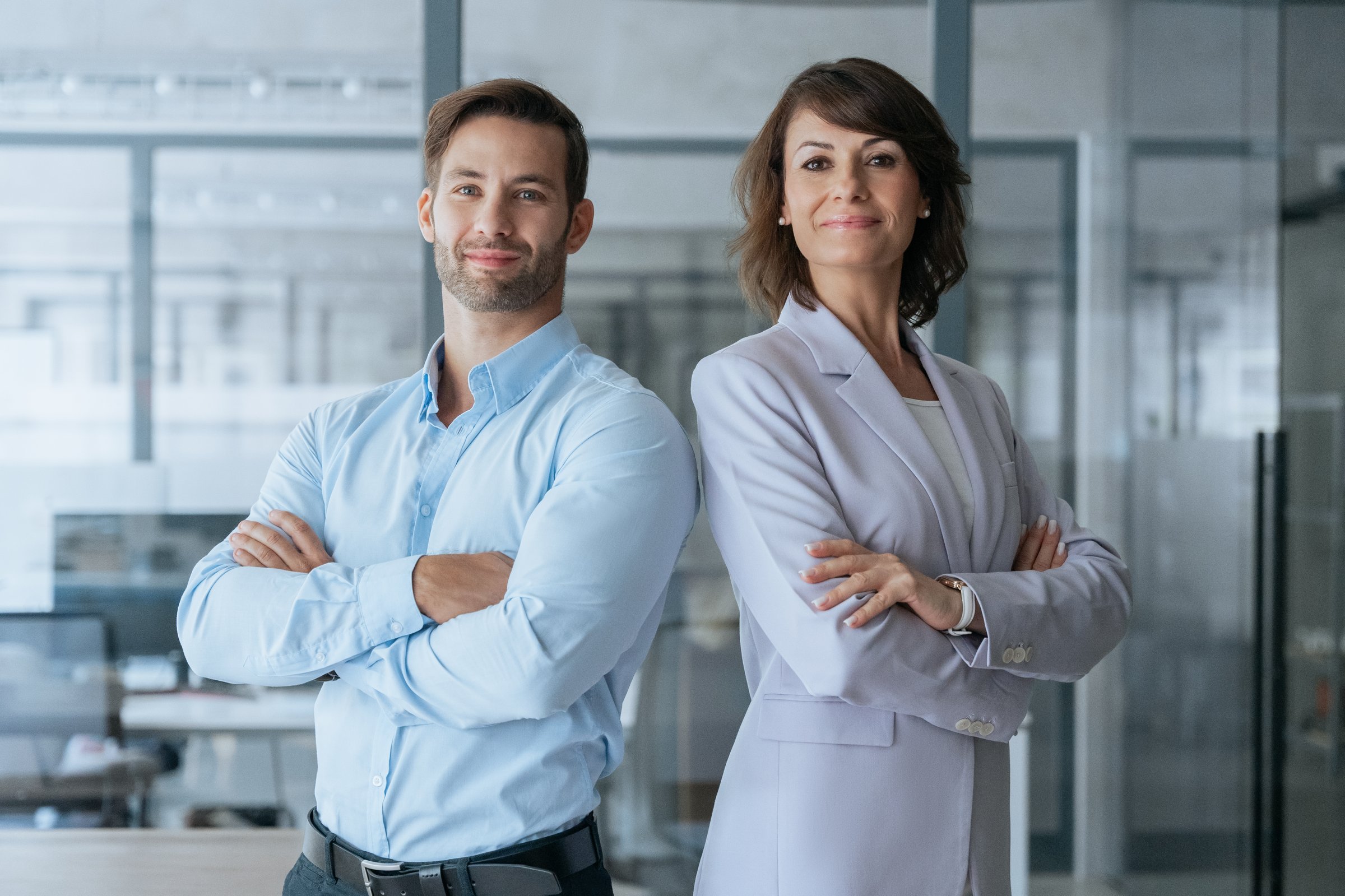 Group team of two confident colleagues professional business people, board of directors. Portrait of young Latin man and European mature leader woman in formal clothes standing arms crossed in office