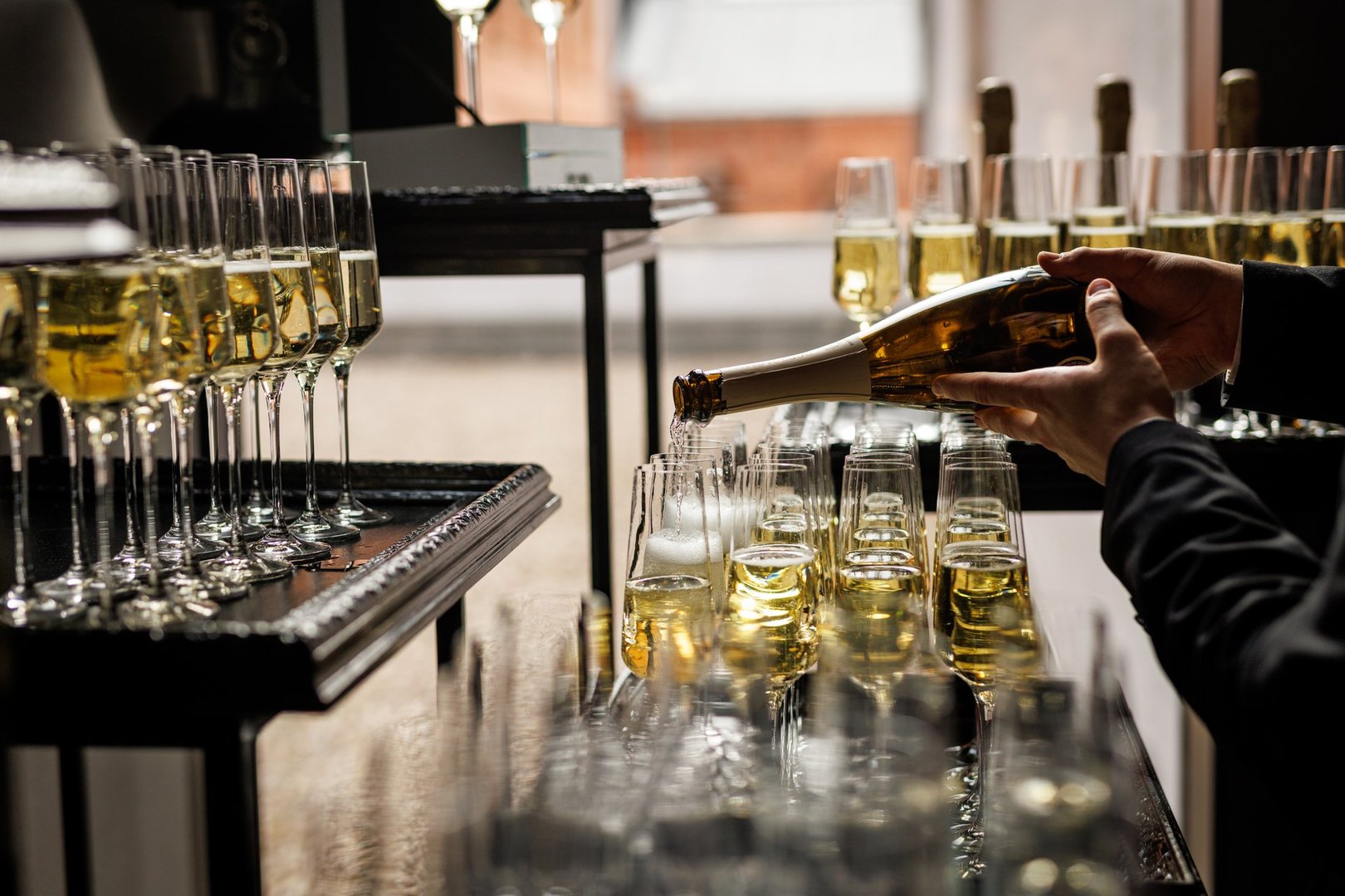 Close-up of a person pouring sparkling champagne into tall flute glasses arranged on a tray during an elegant celebration or reception.