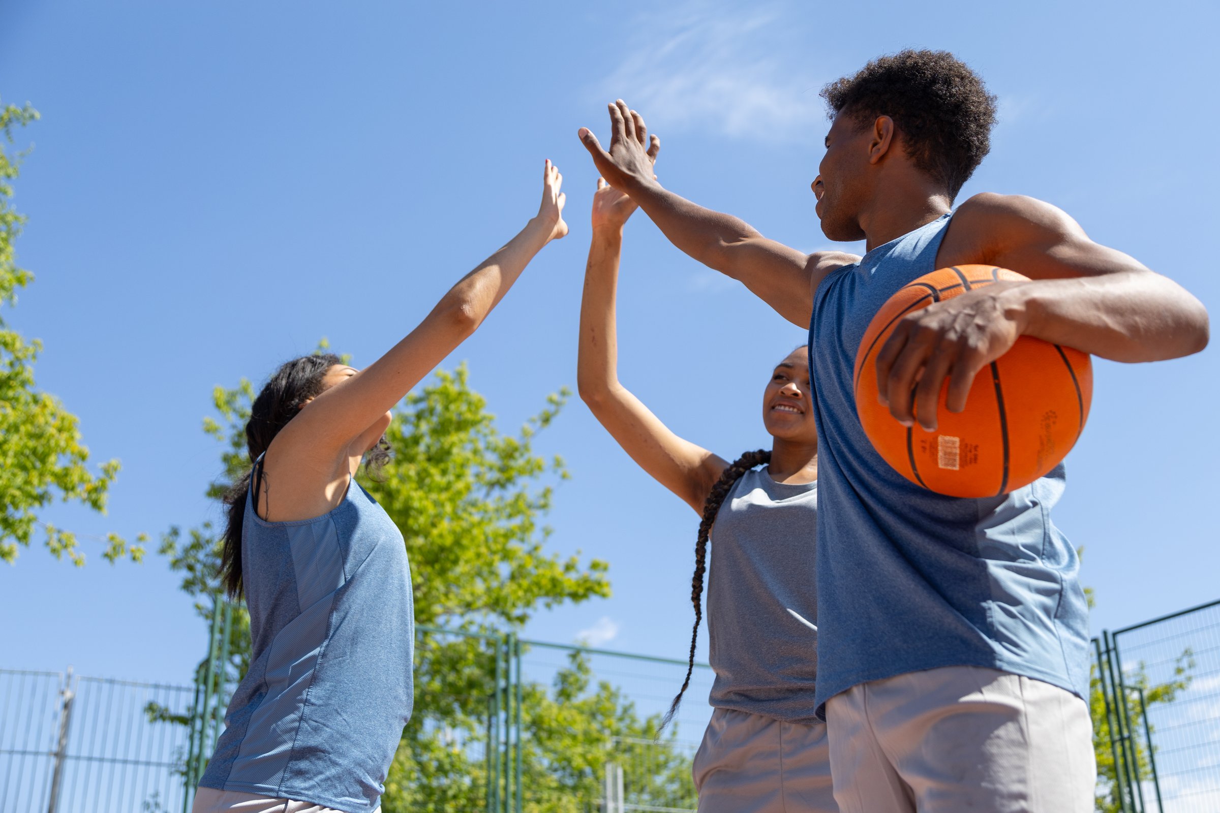 Basketball players celebrating victory, giving high five on outdoor court, demonstrating teamwork and sportsmanship