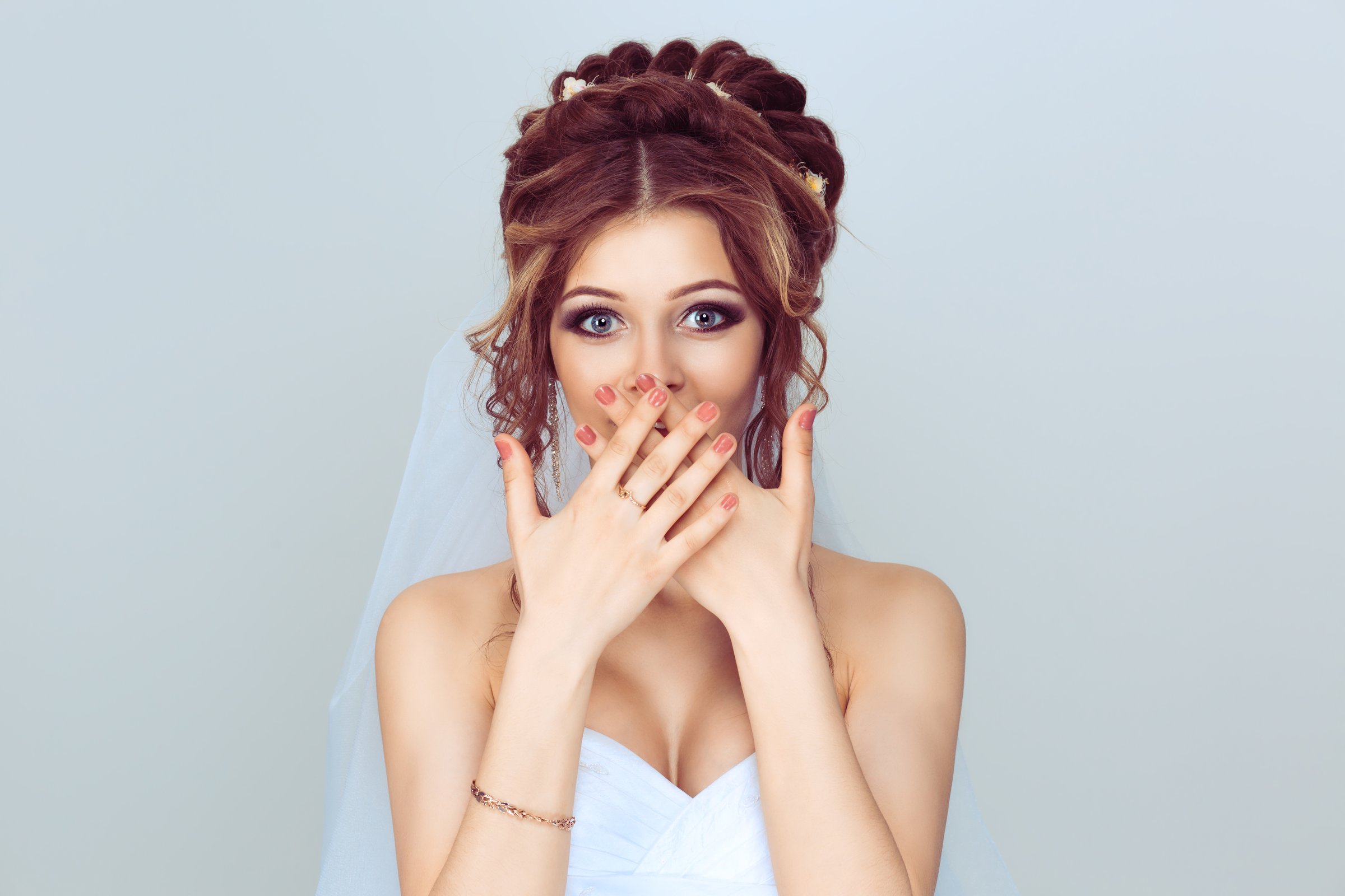 OMG. Pretty beautiful excited surprised woman bride girl covering her open mouth with hands, over light blue background. Positive face expression